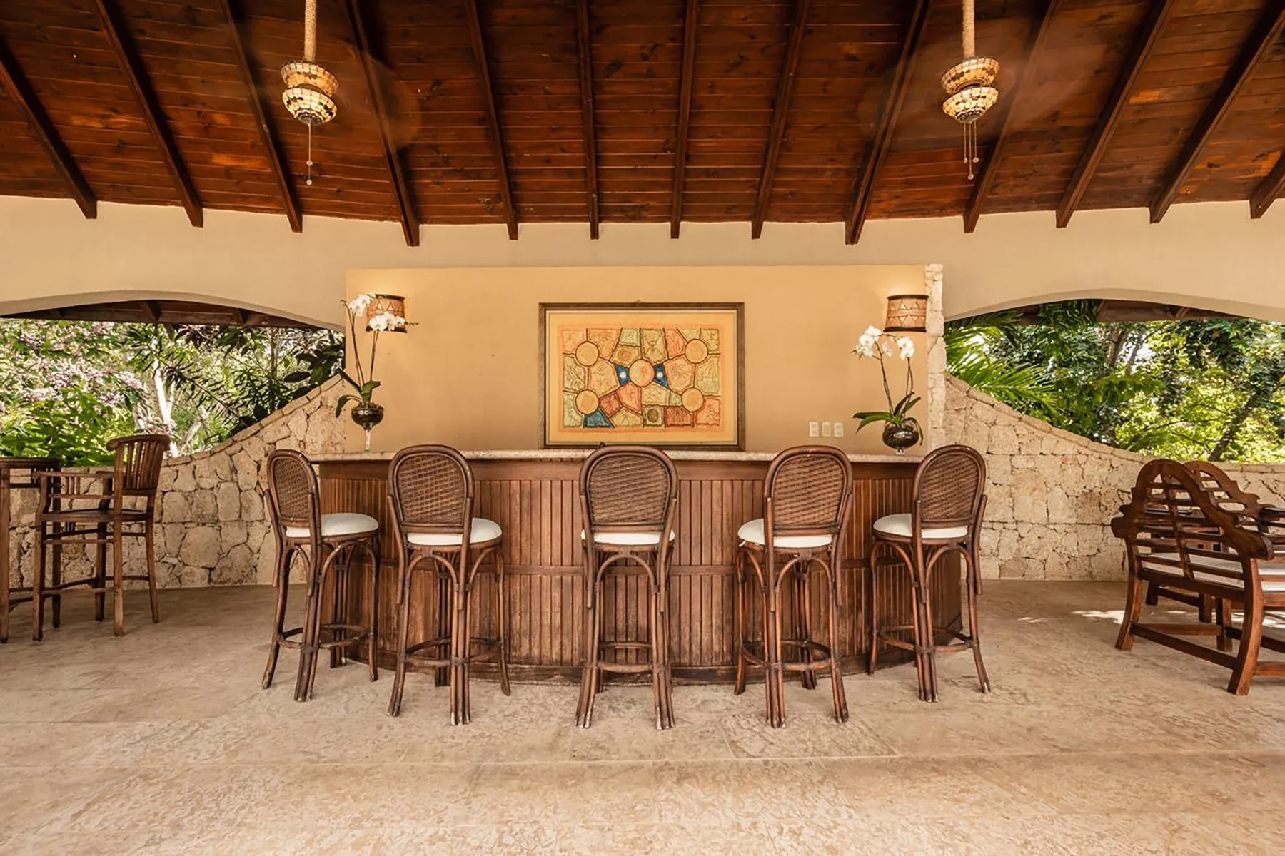 An open-air bar with tall seating, stone walls, and a wooden ceiling.
