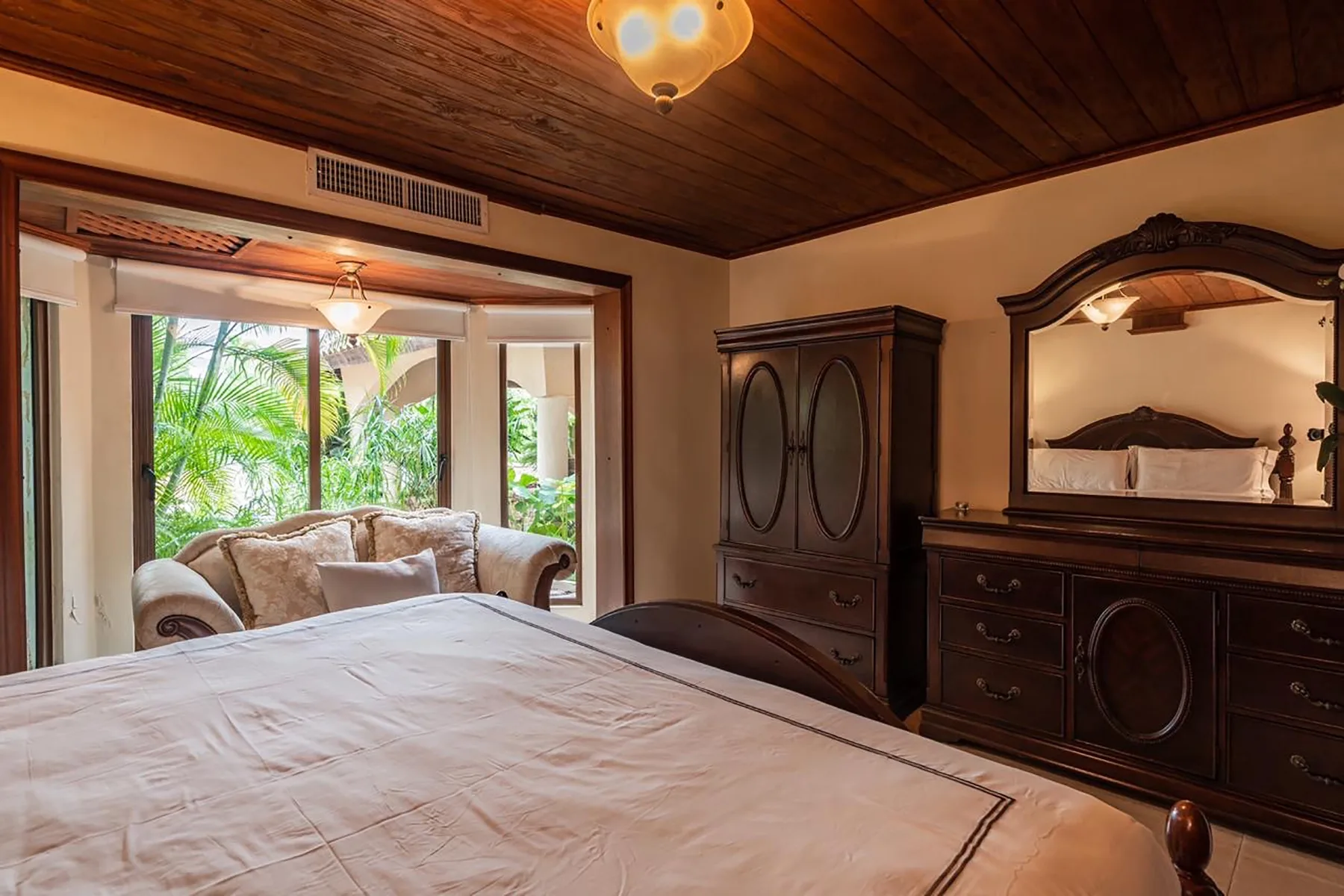 A bedroom with a large bed, dark wooden furniture, and a bright sitting area.