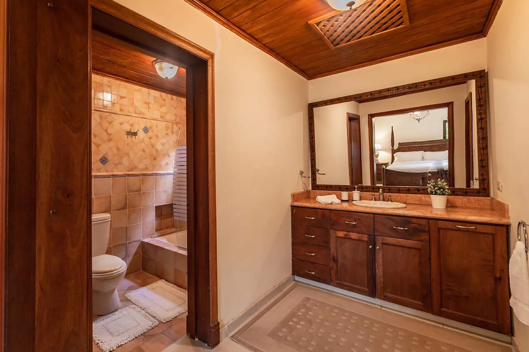 A bathroom vanity with a large mirror stands beside an open doorway to a tiled shower area.