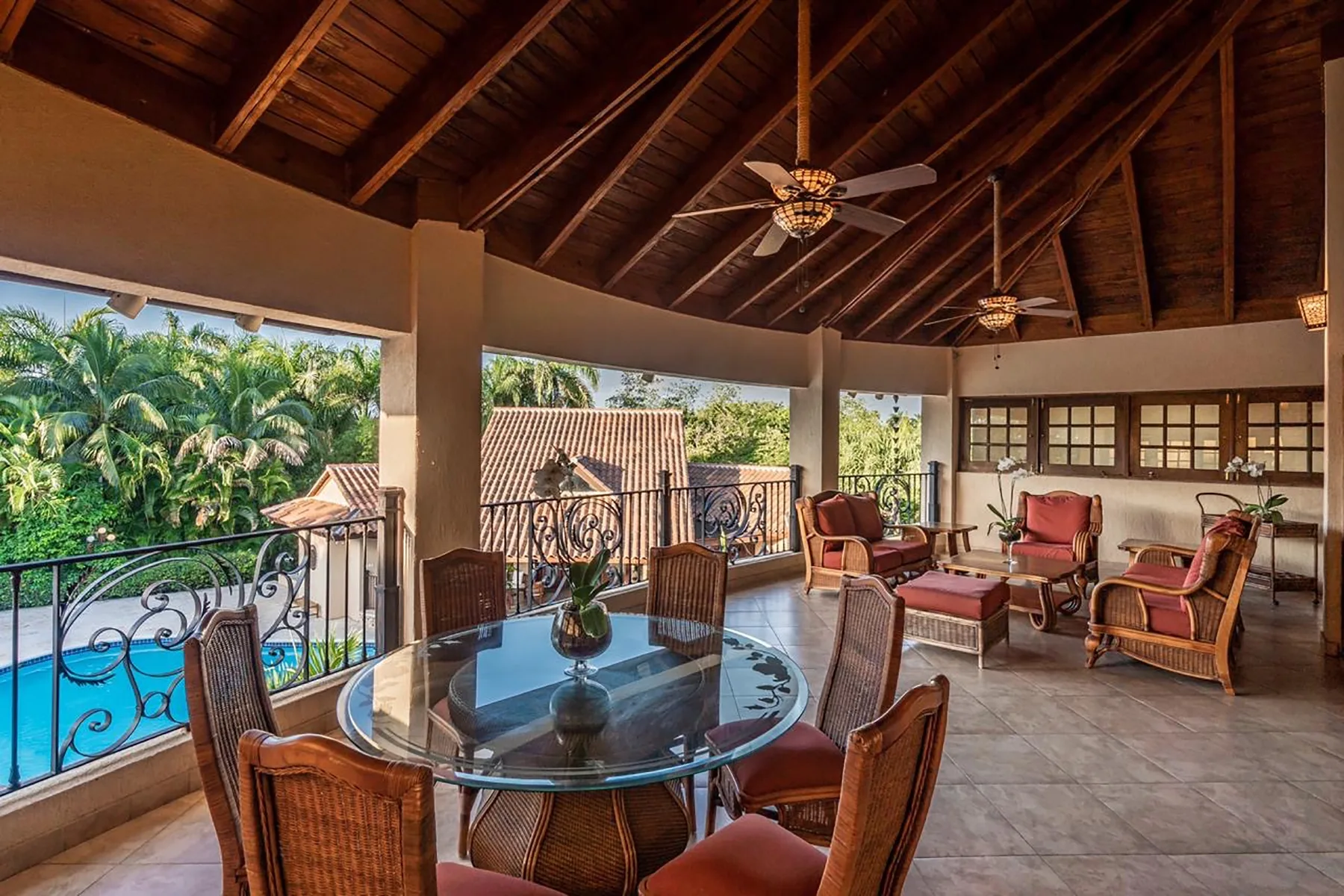 An open-air lounge and dining area with a glass table and views of a pool.