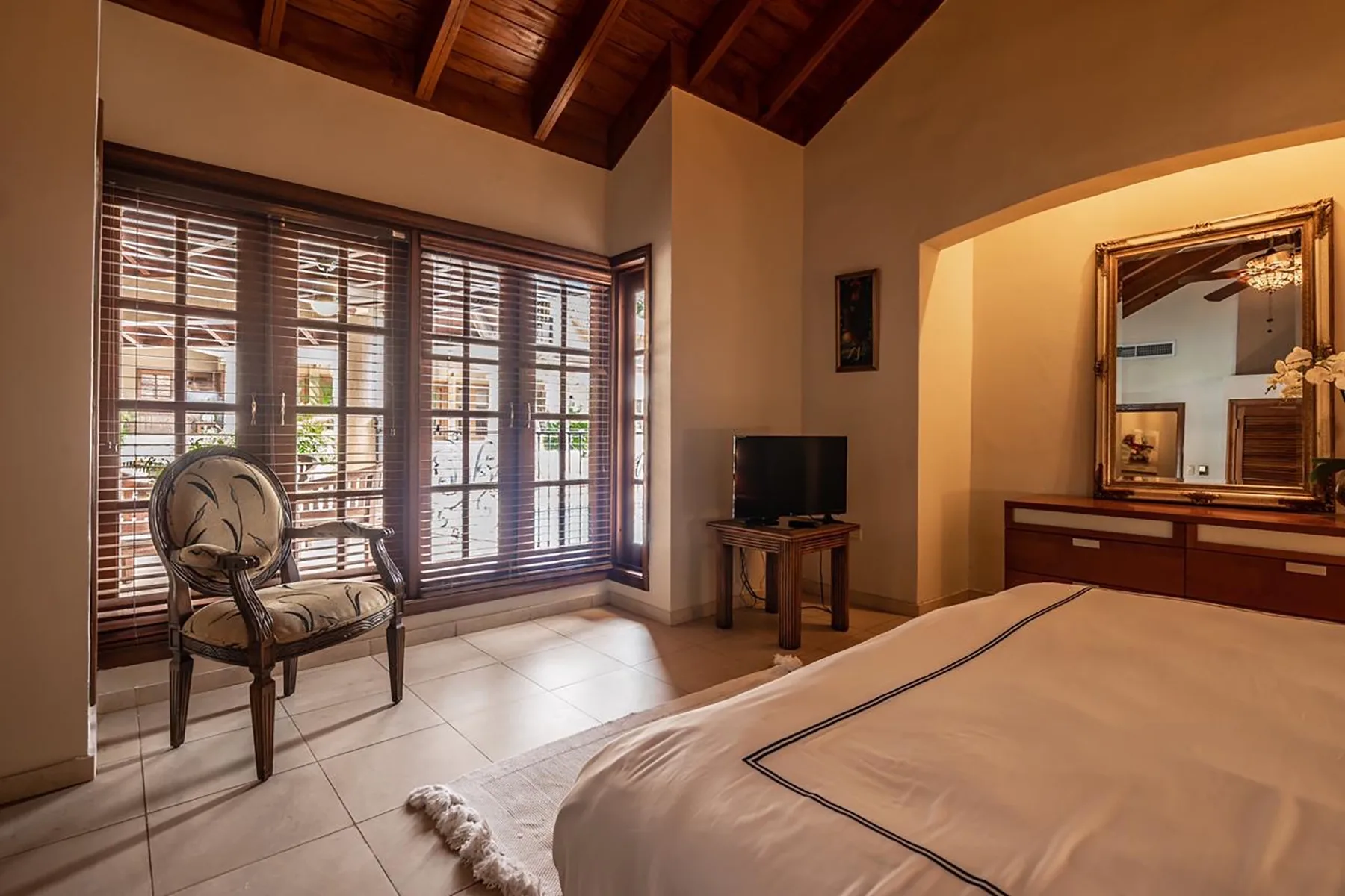A bedroom with a large bed, a television, and windows with wooden blinds.