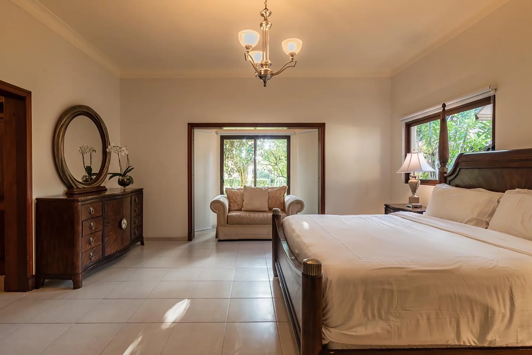 A bedroom with a large bed, a dresser, and a window overlooking greenery.