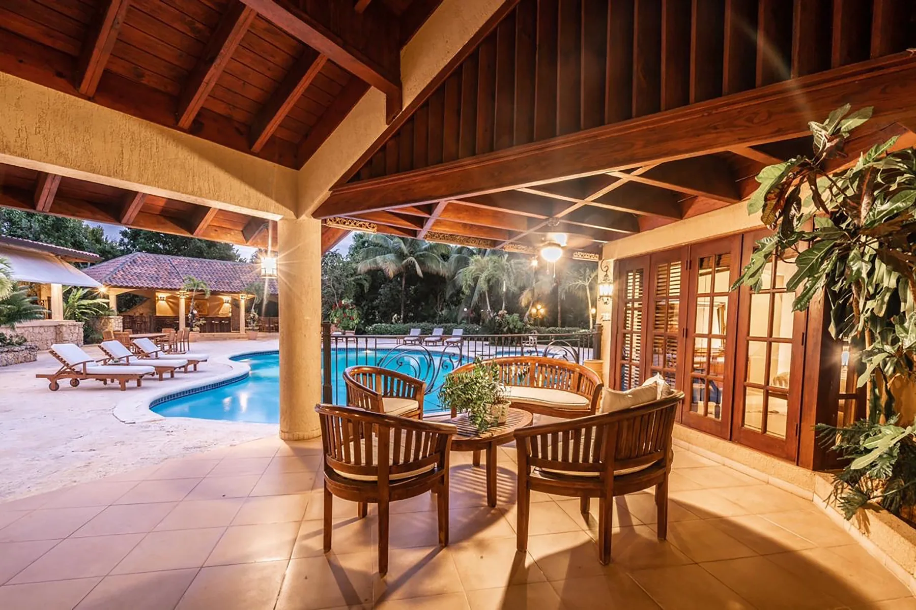 A covered outdoor dining area overlooks a swimming pool and lounge seating.