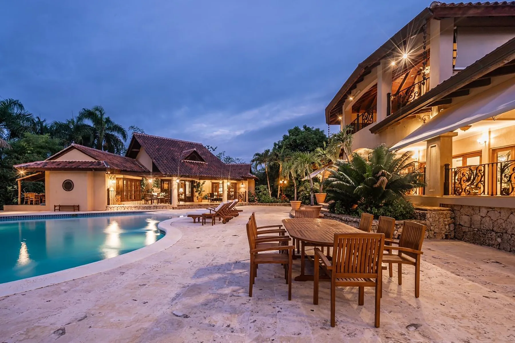 A poolside patio with outdoor seating beside a warmly lit building at dusk.