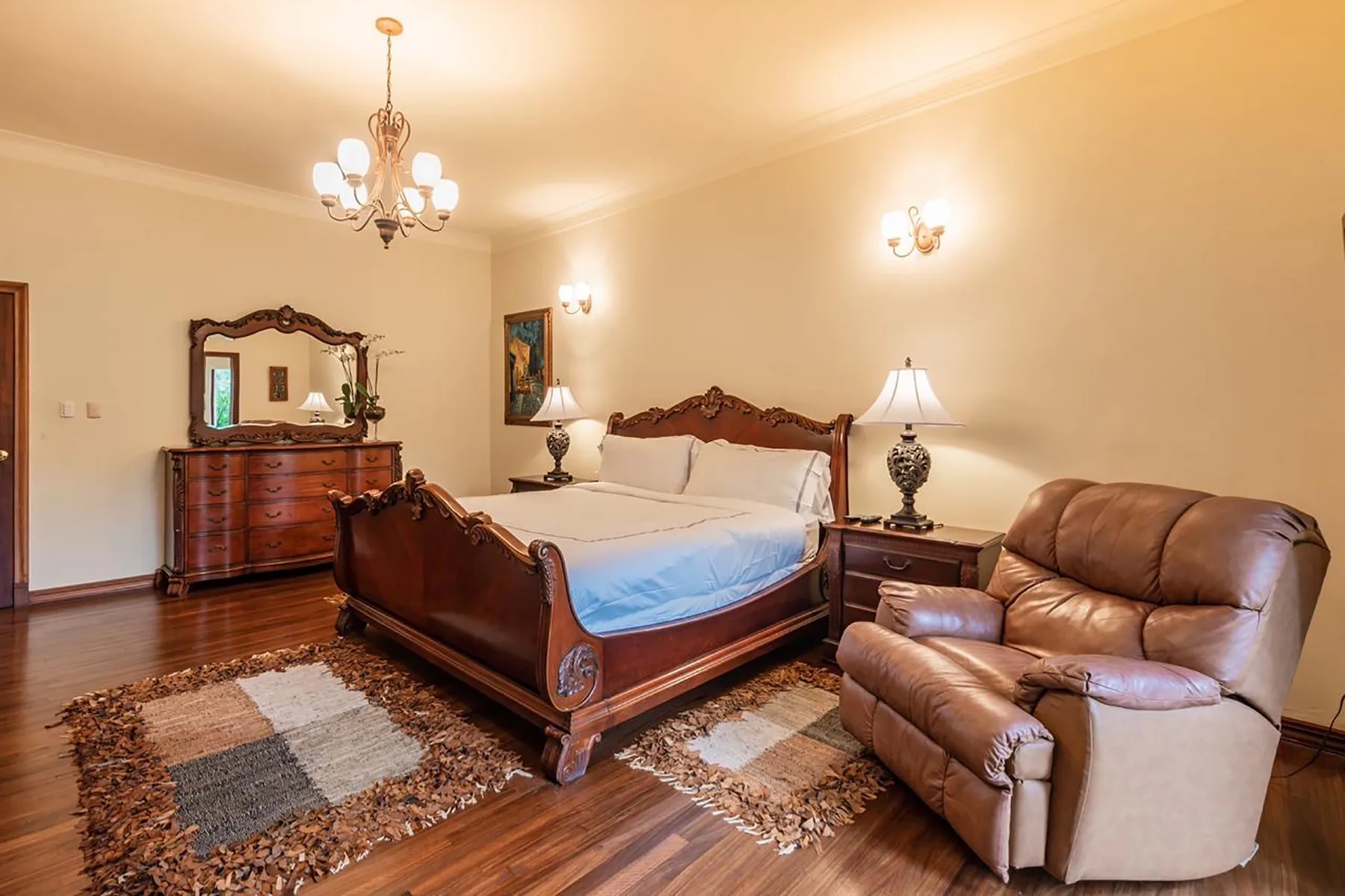 A bedroom with a carved wooden bed and leather seating.
