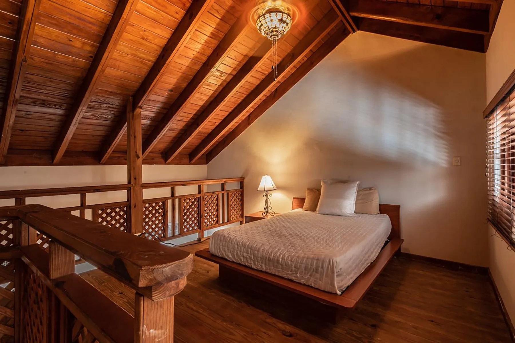 A bedroom with a bed beneath a sloped wooden ceiling and exposed beams.