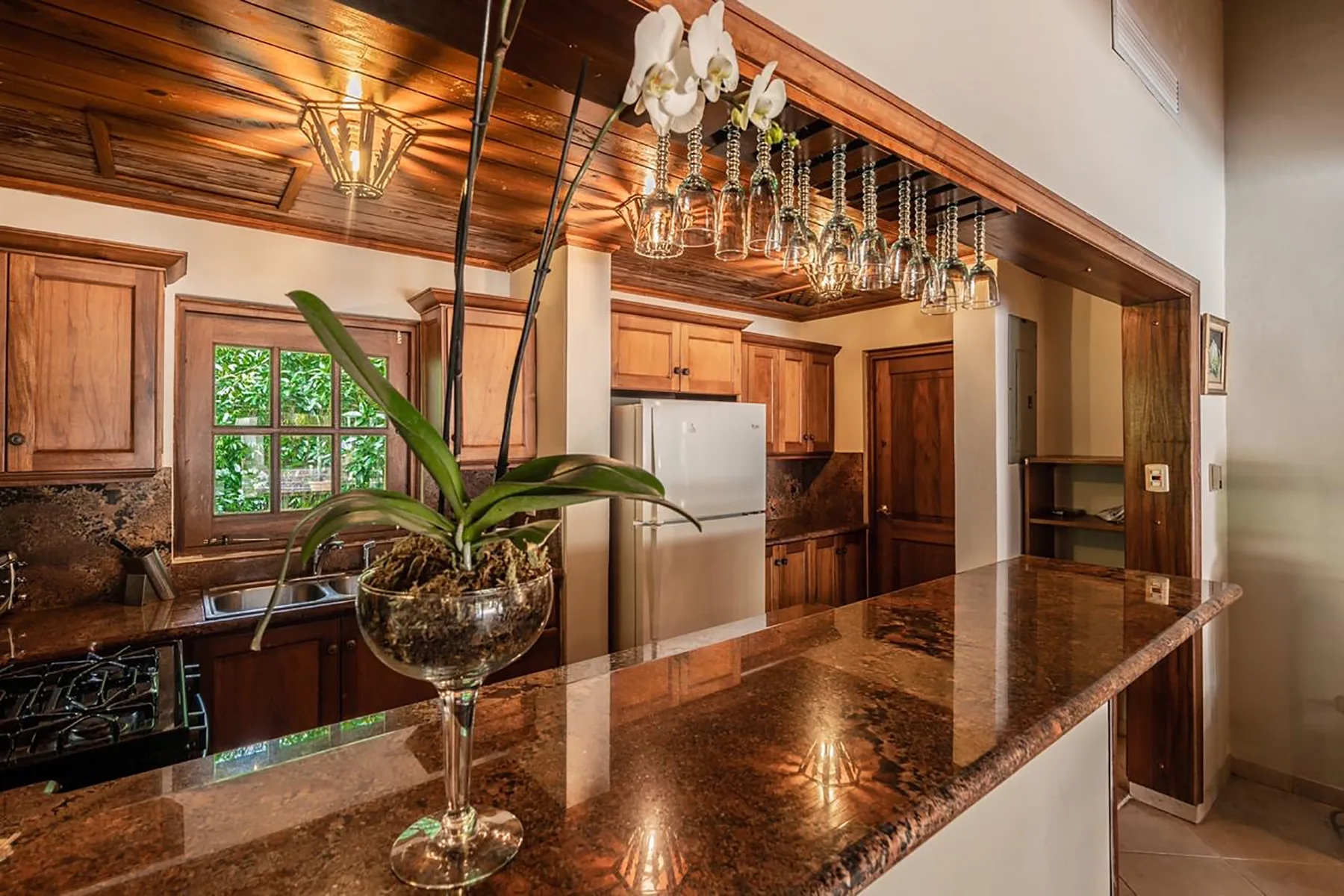 A kitchen with wooden cabinetry, a stone island, and hanging glassware.