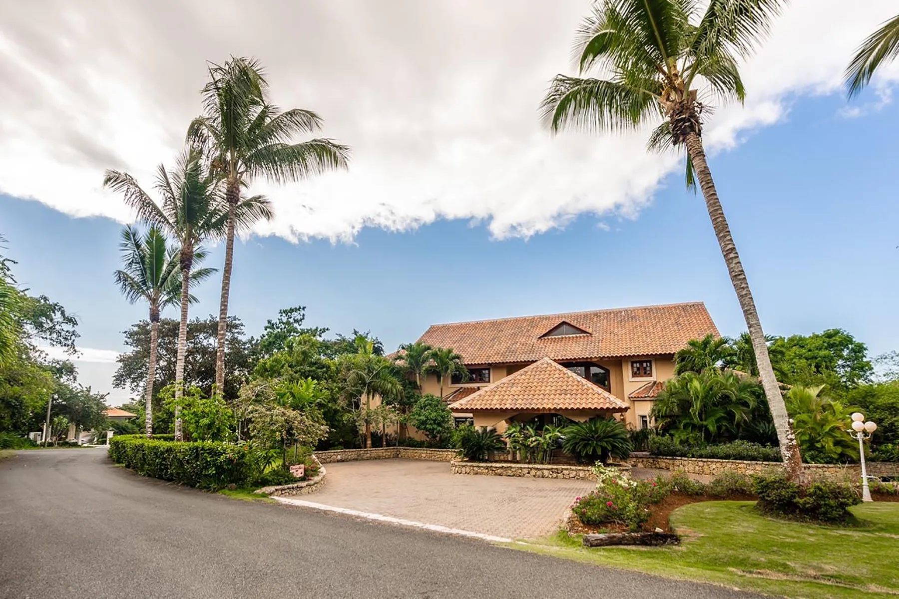 A tropical property entrance with a tiled-roof building, palm trees, and landscaped grounds.