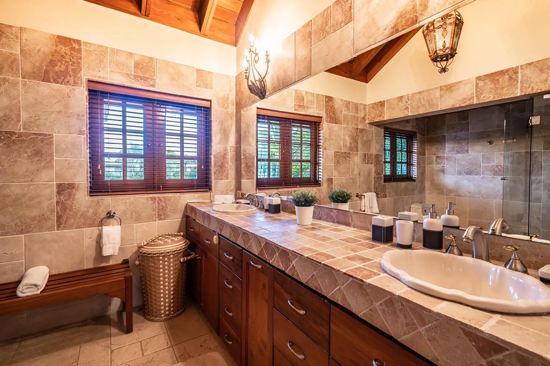 A tiled bathroom with a long counter, sinks, and windows.