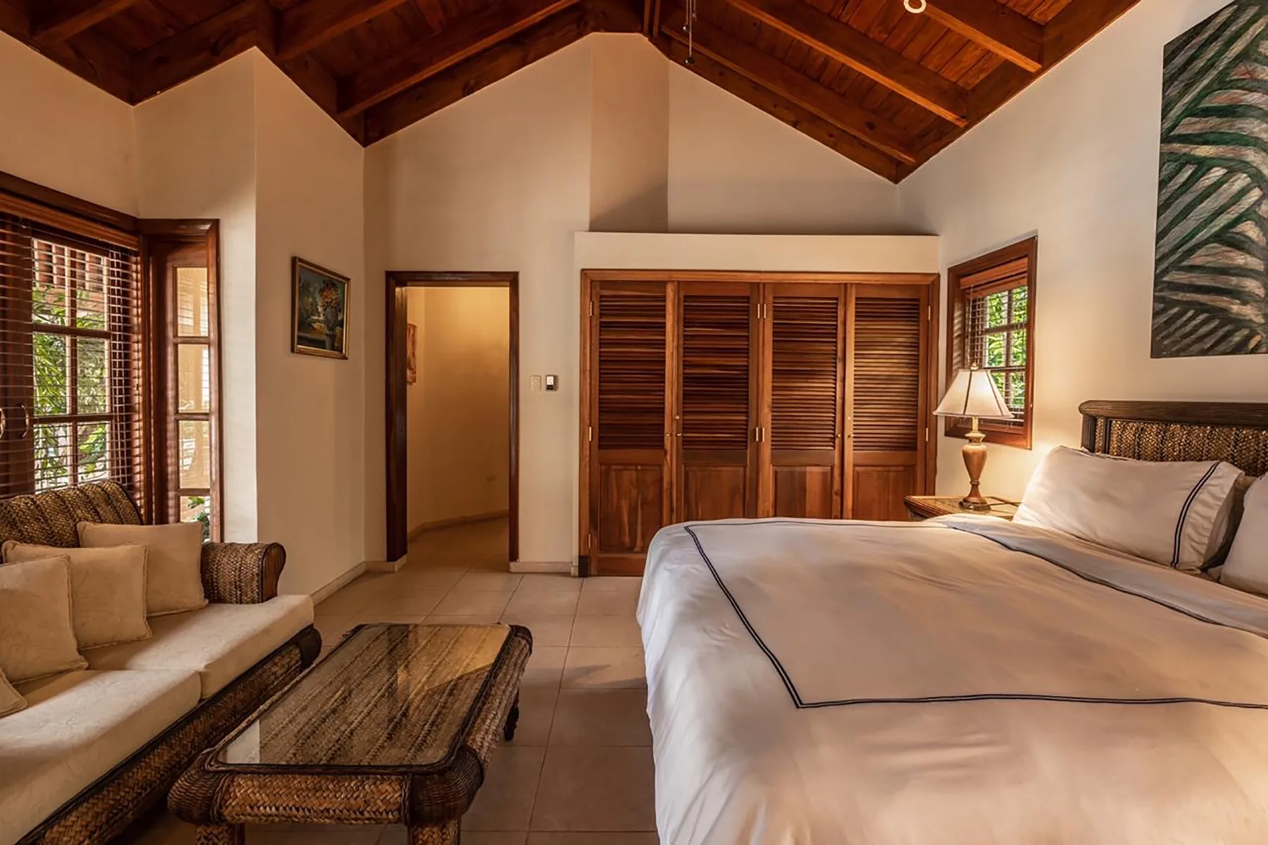 A bedroom with a large bed, a seating area, and wooden doors beneath a sloped ceiling.