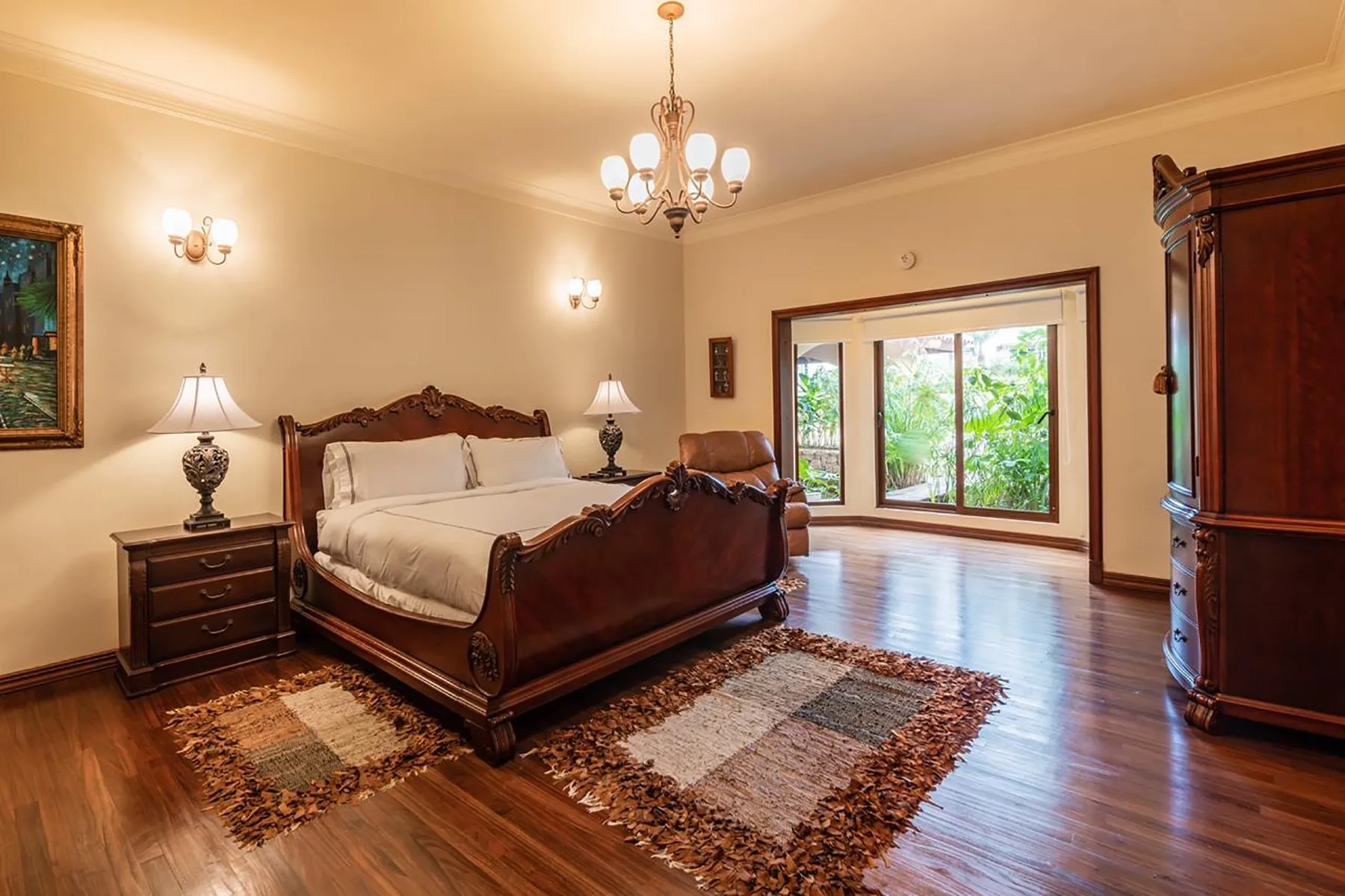 A warmly lit bedroom with a large bed, bedside tables, and a window overlooking greenery.