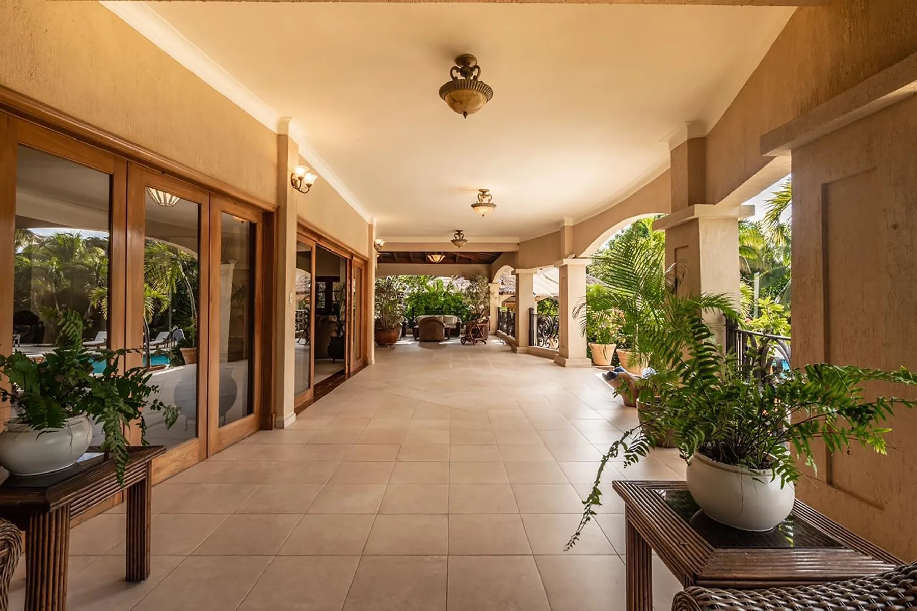 A covered patio with tiled flooring, glass doors, and potted plants.
