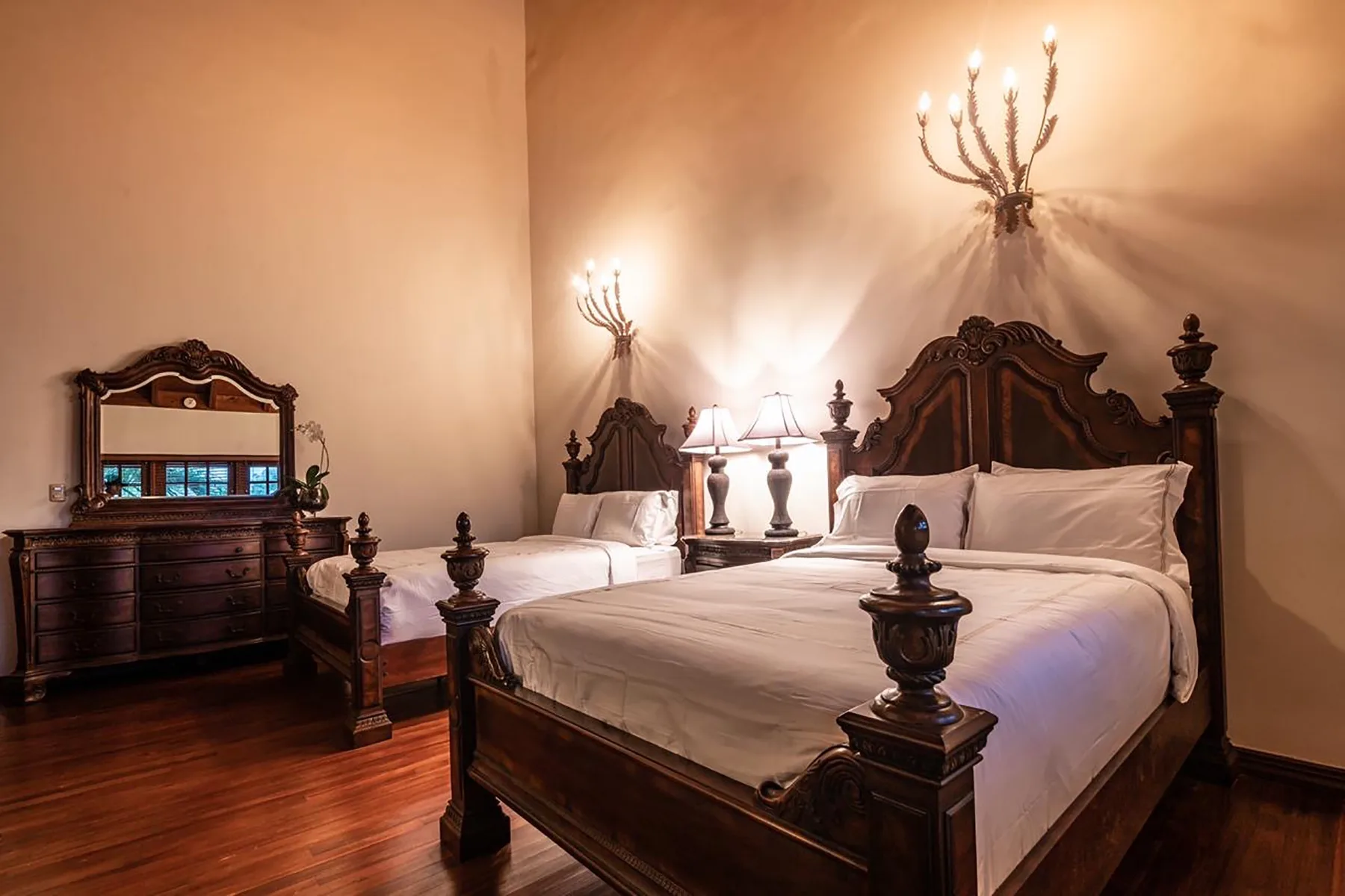 A bedroom with two beds and dark wood furnishings.
