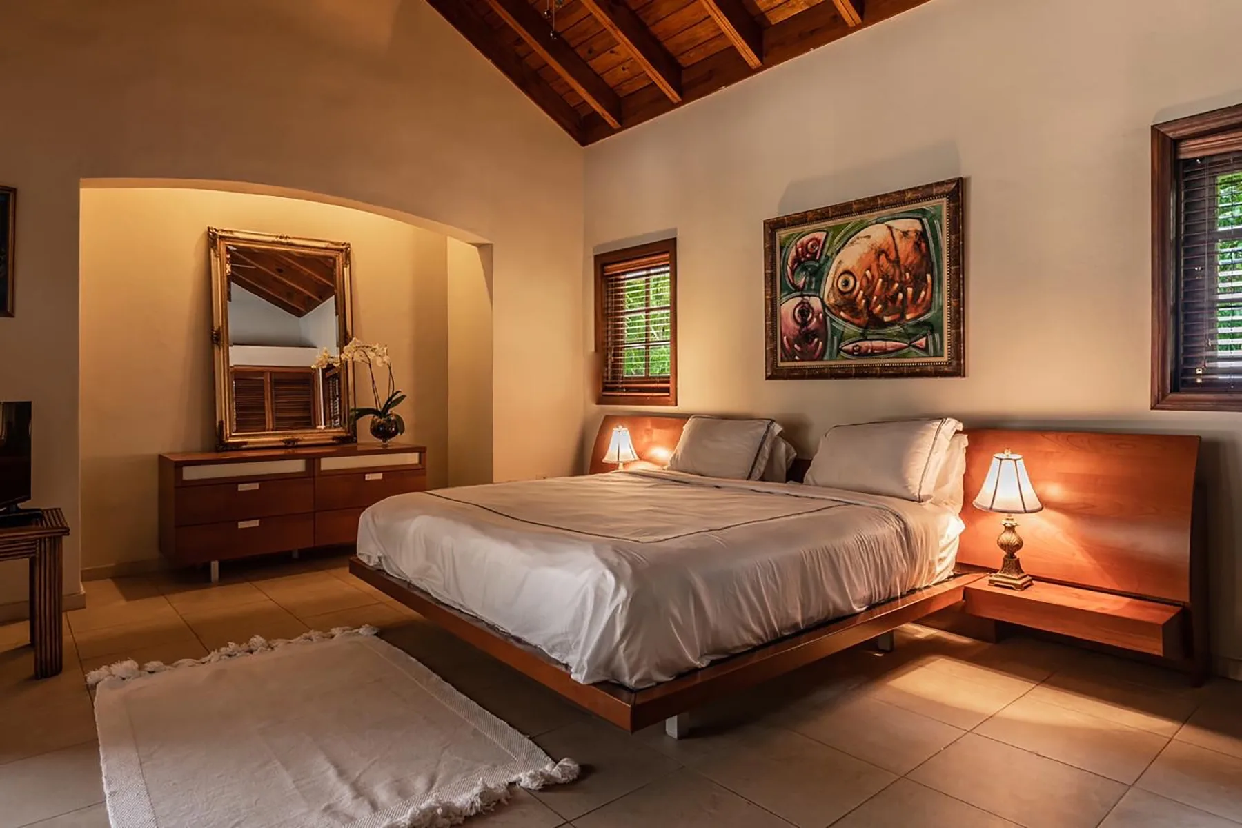 A bedroom with a large bed, bedside lamps, and framed artwork.