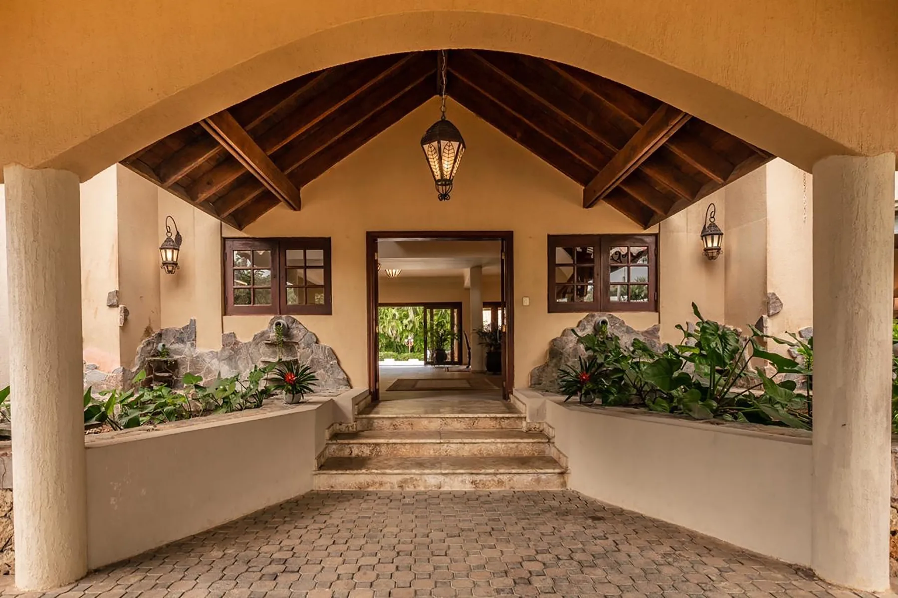 A covered entryway with a timber ceiling, hanging lanterns, and planted beds.