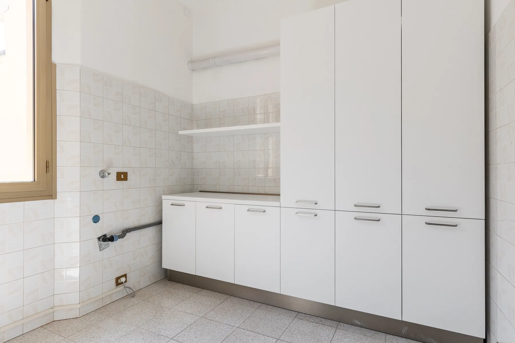 A tiled kitchen with white cabinets and a window.