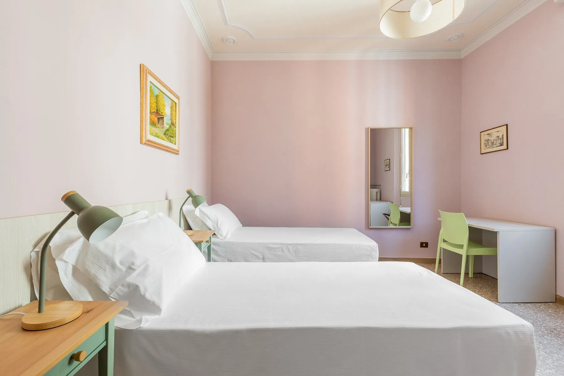 A bedroom with two beds, bedside lamps, and a small desk.