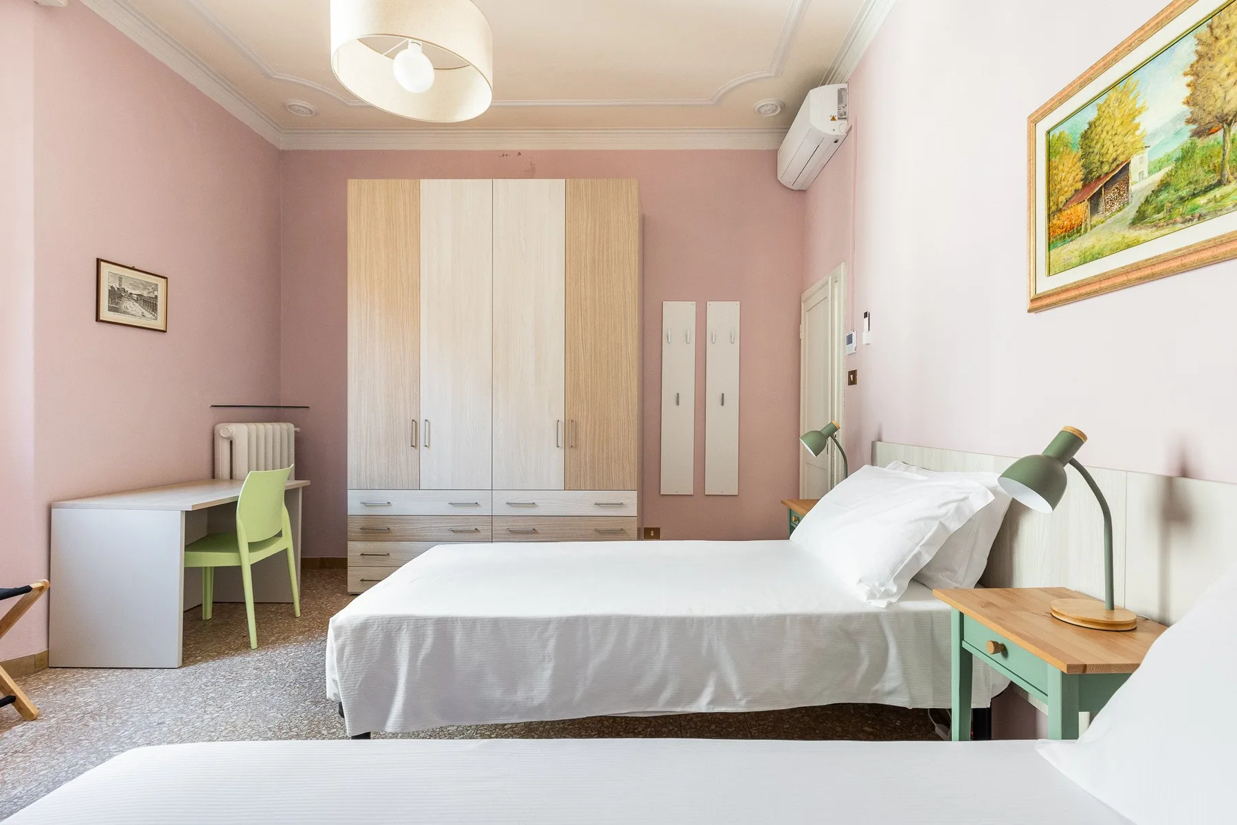 A bedroom with two beds and a wardrobe, desk, and bedside table.