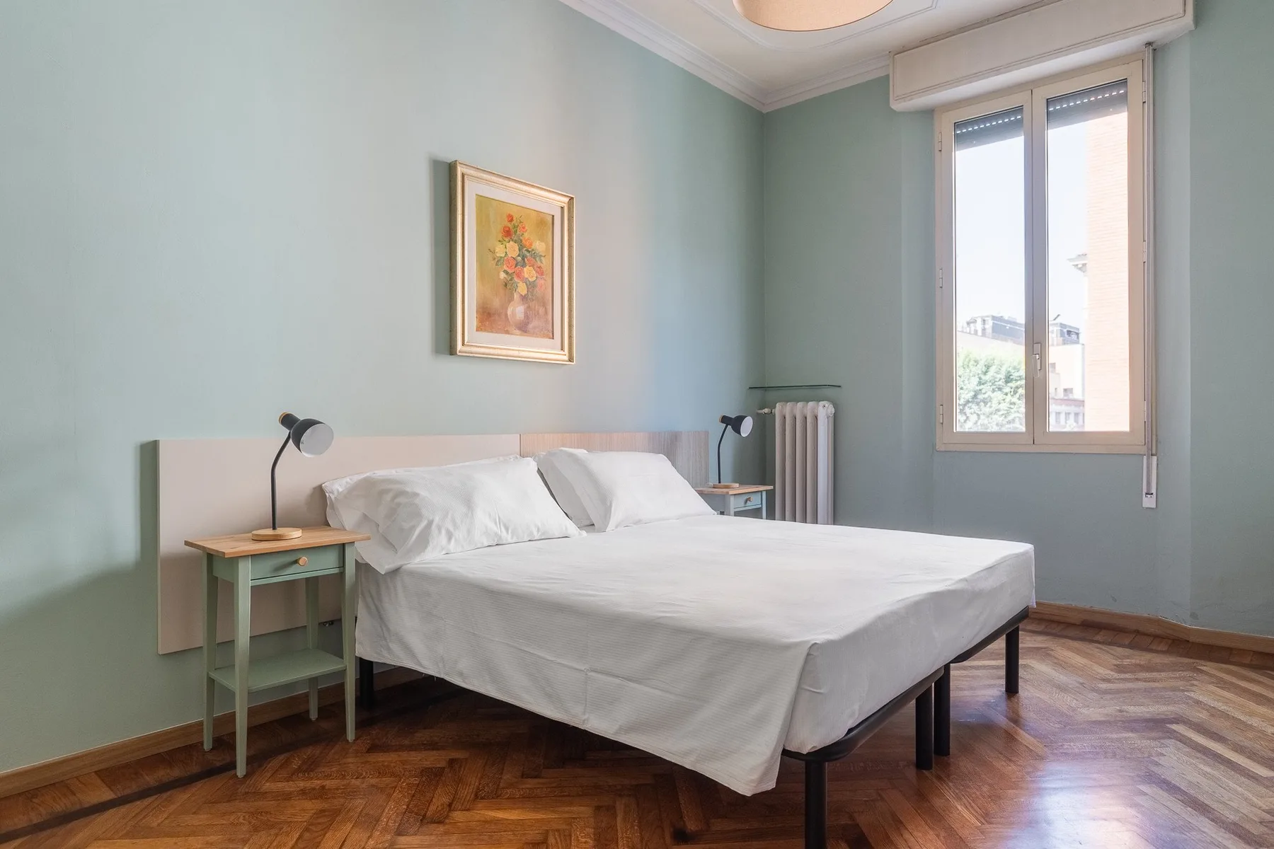 A bedroom with a neatly made bed and a tall window.