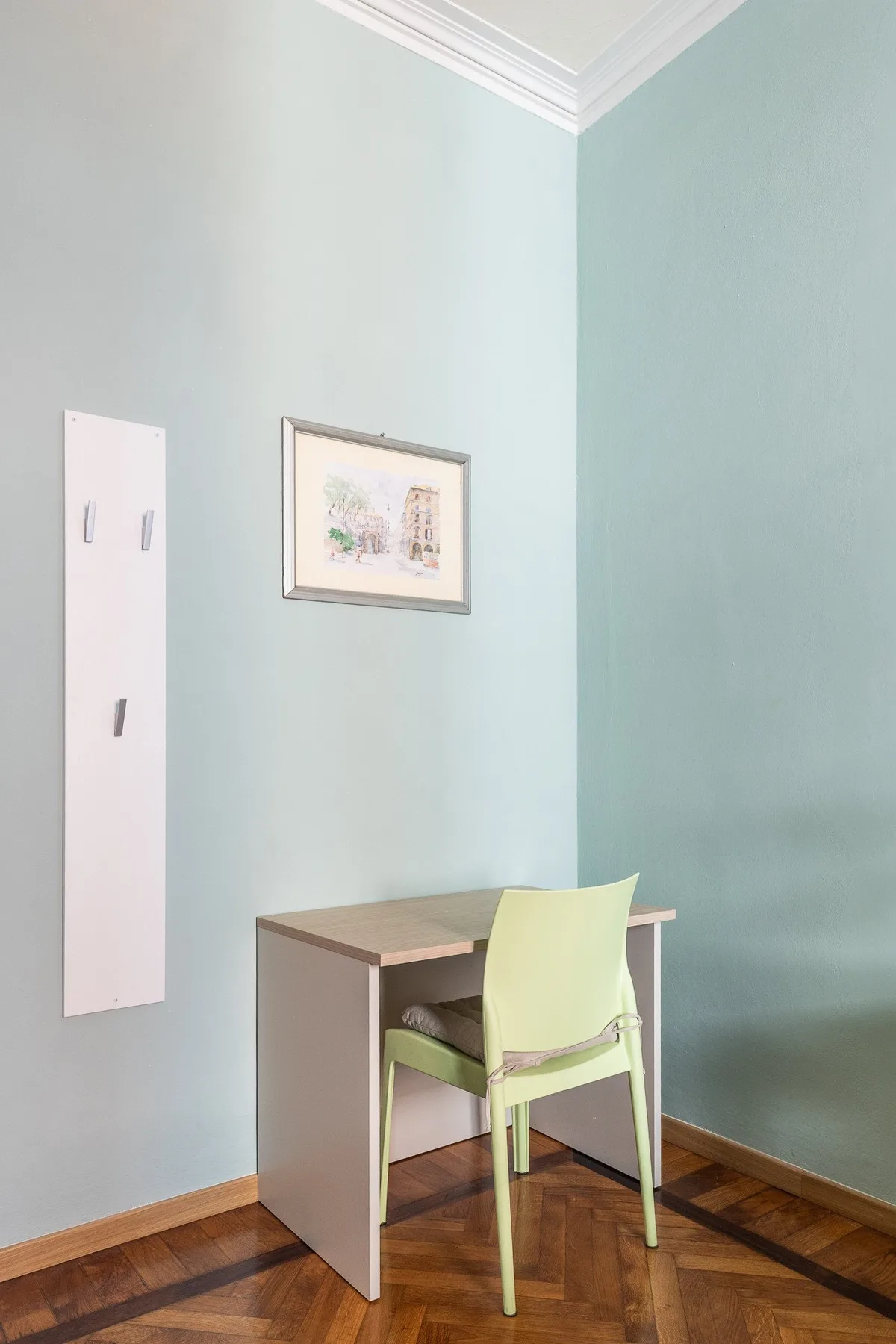 A small desk and chair sit against pale blue walls in a bright room.
