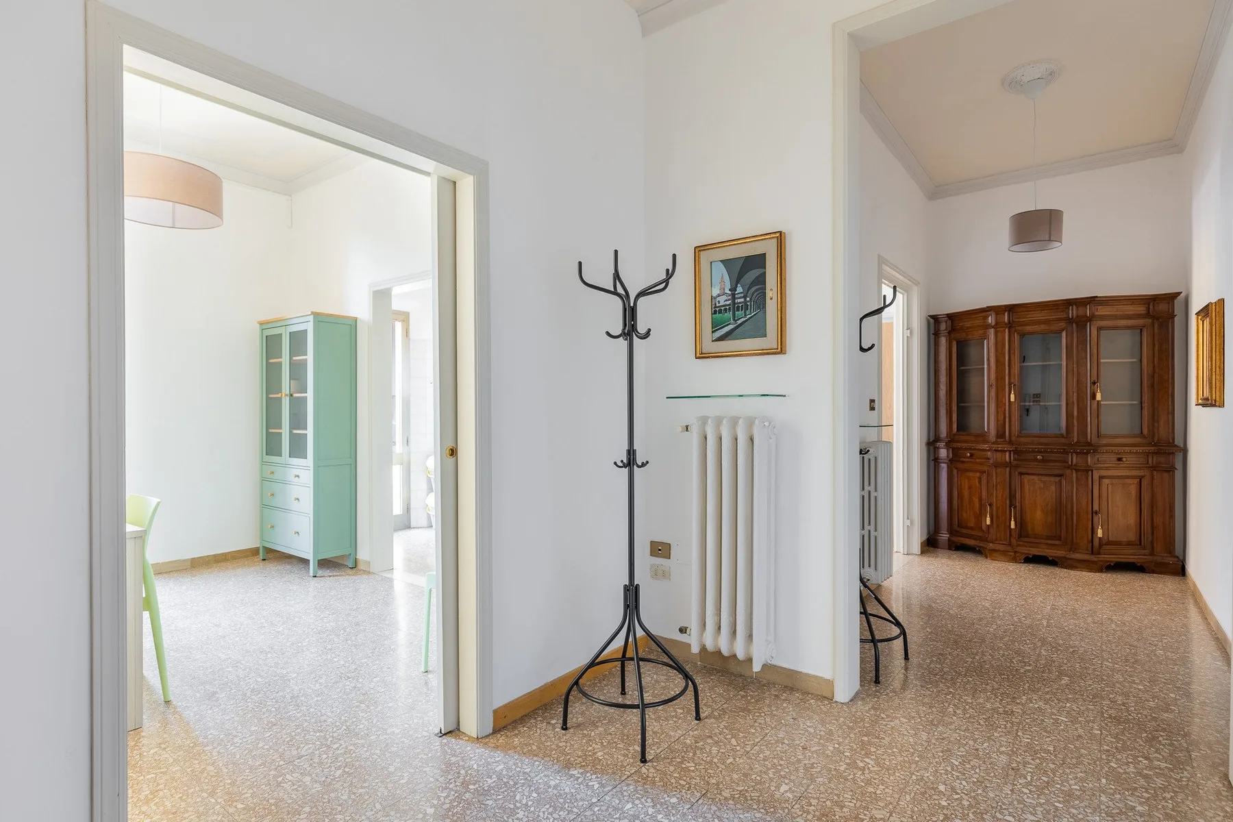 A bright interior hallway opens onto adjoining rooms with a coat rack and wooden cabinet.