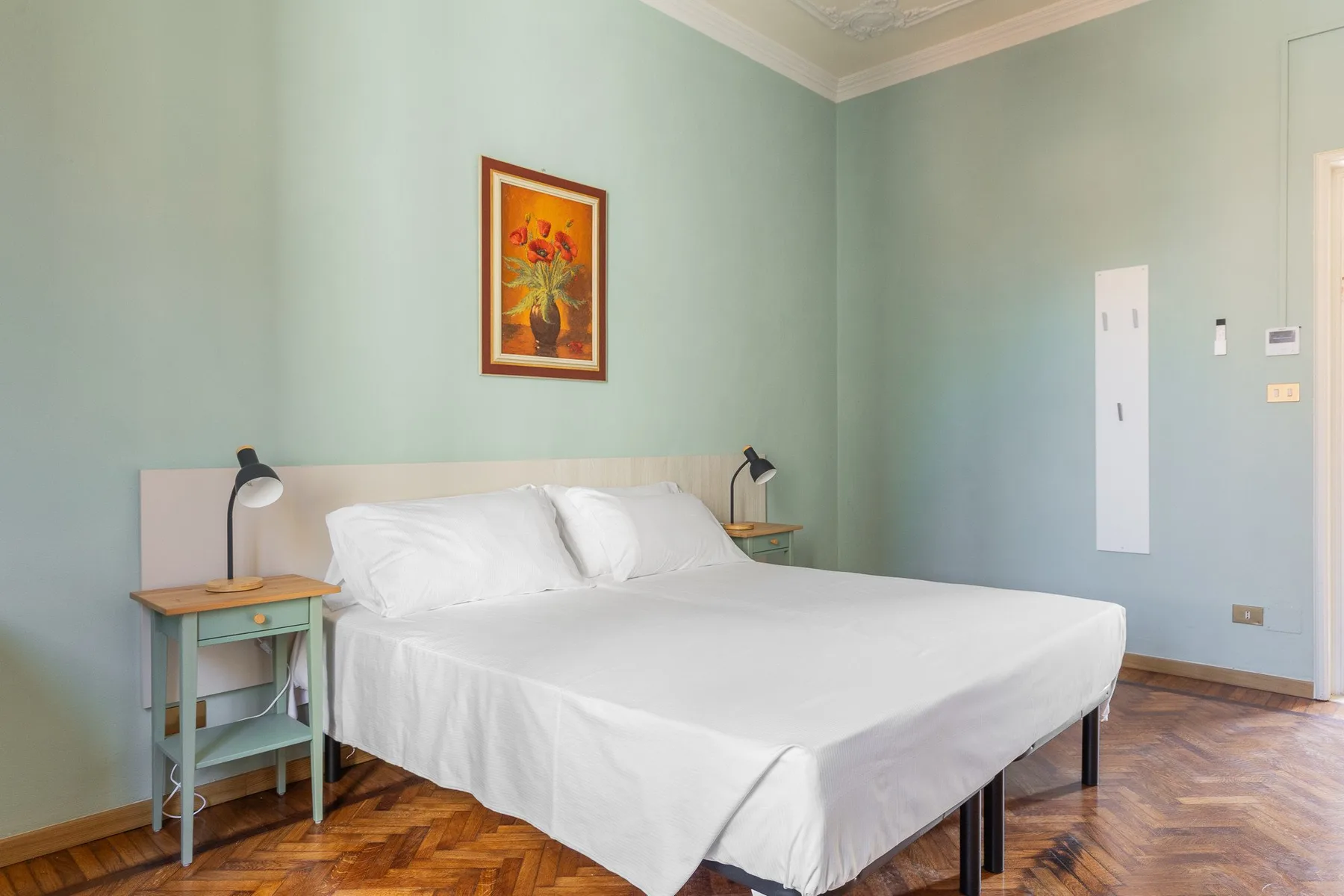 A bedroom with a bed, bedside tables, and a framed floral painting.