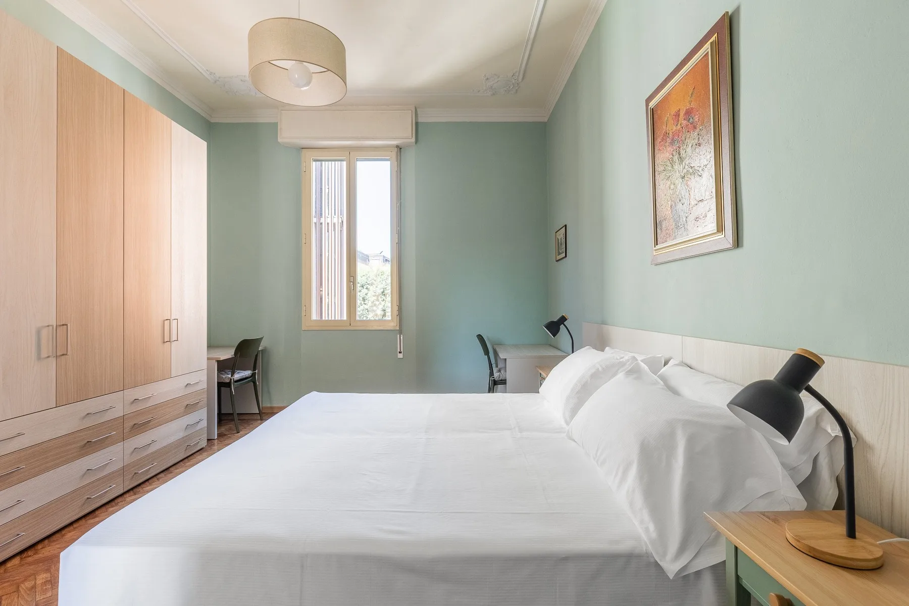 A bedroom with a neatly made bed, wardrobes, and a window.