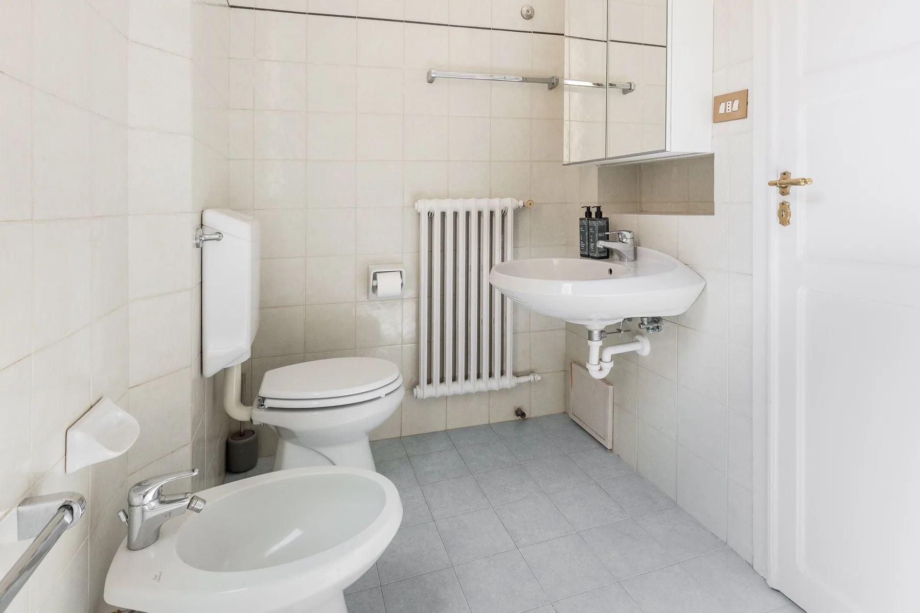 A tiled bathroom with a toilet, bidet, and wall-mounted sink.