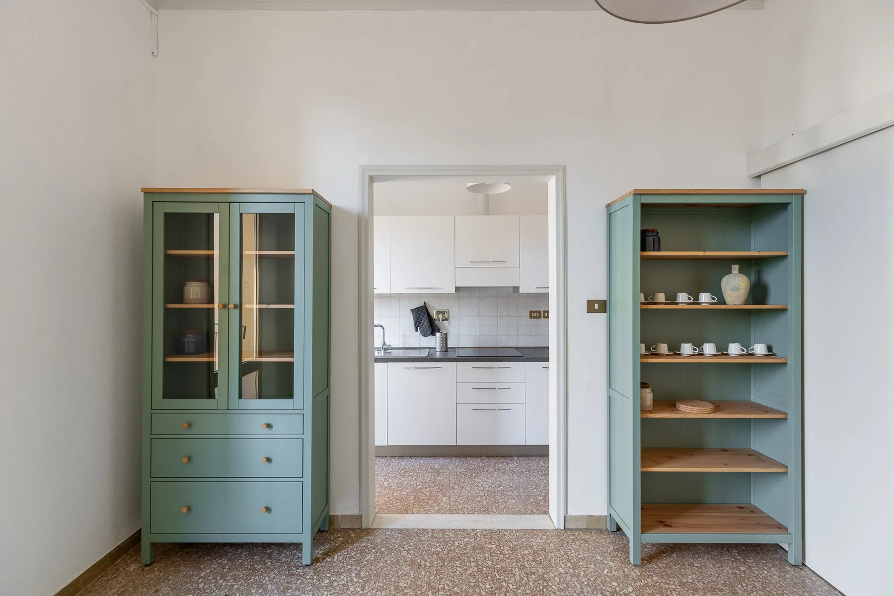 A kitchen is visible through a doorway between two green cabinets.
