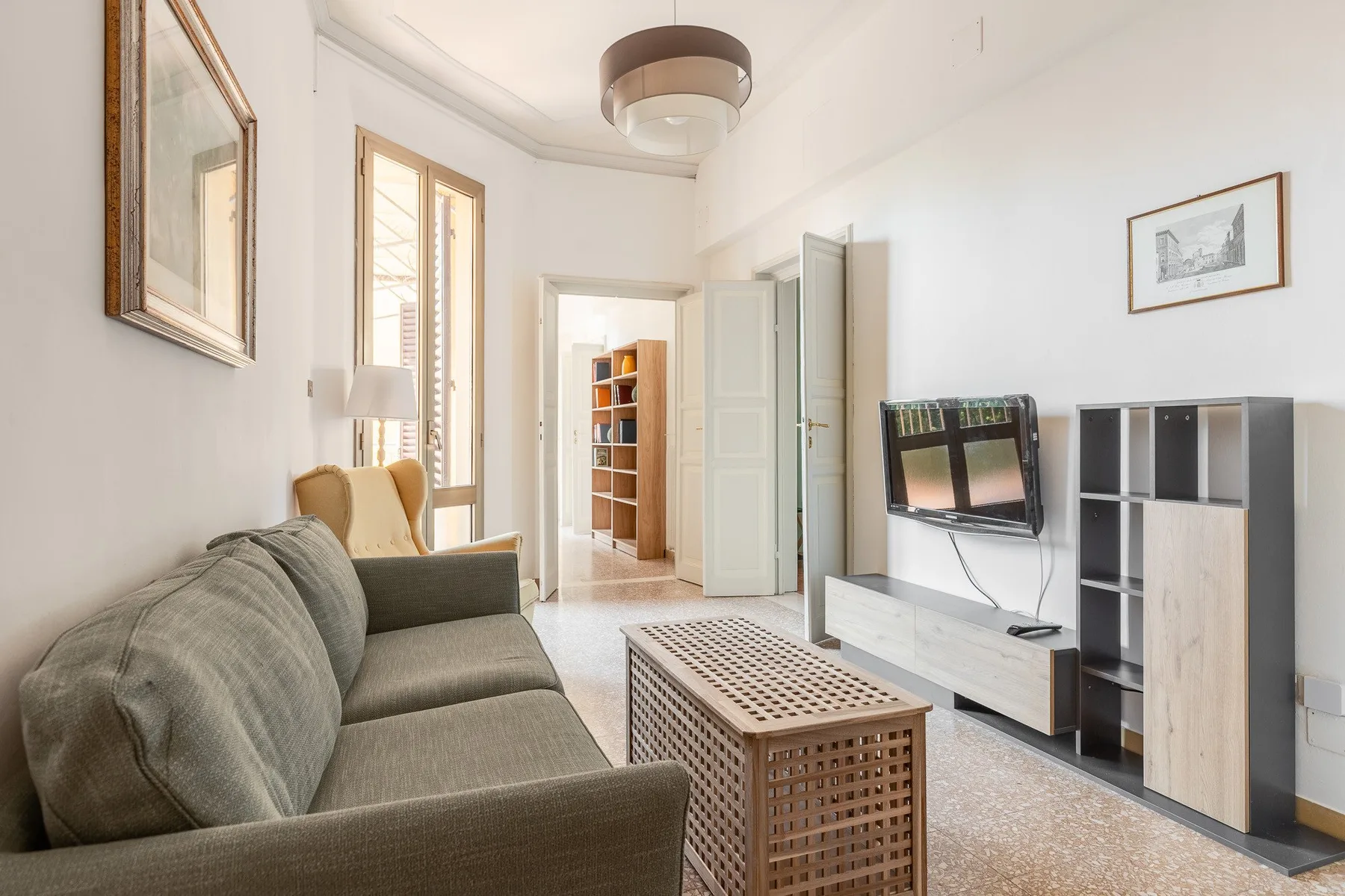 A bright living room with seating, a television, and shelving.