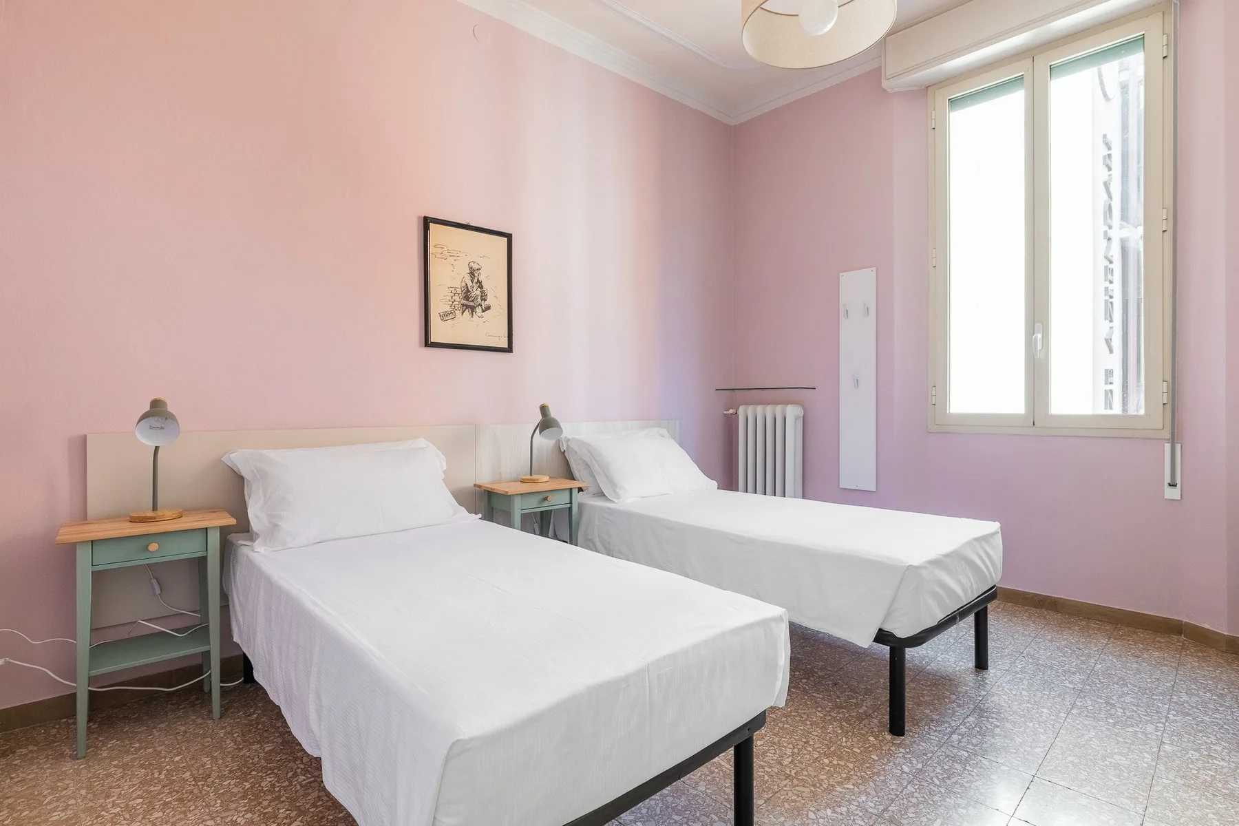 A pink bedroom with two single beds, bedside tables, and a tall window.