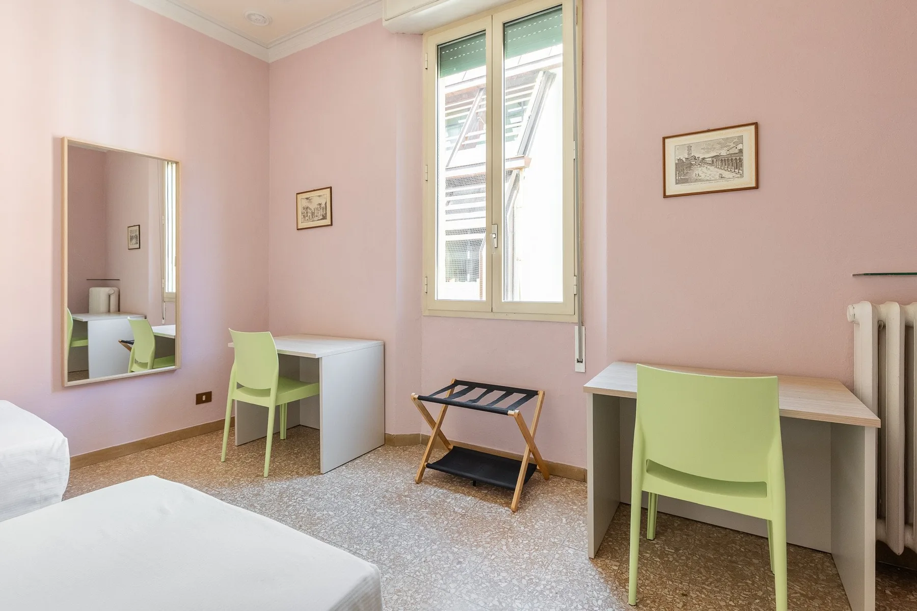 A pink bedroom with two desks, green chairs, and a window.