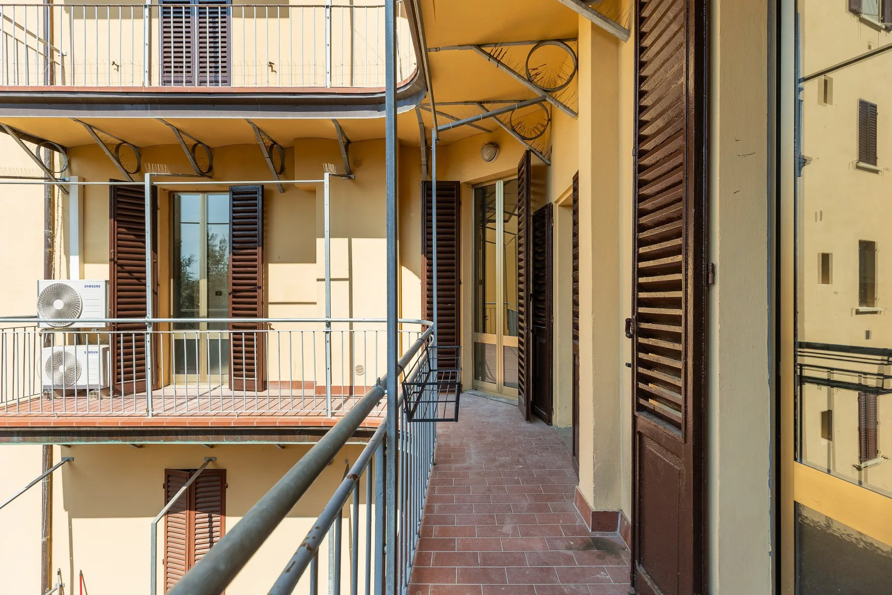 An open-air apartment corridor with tiled flooring and doors along the walls.
