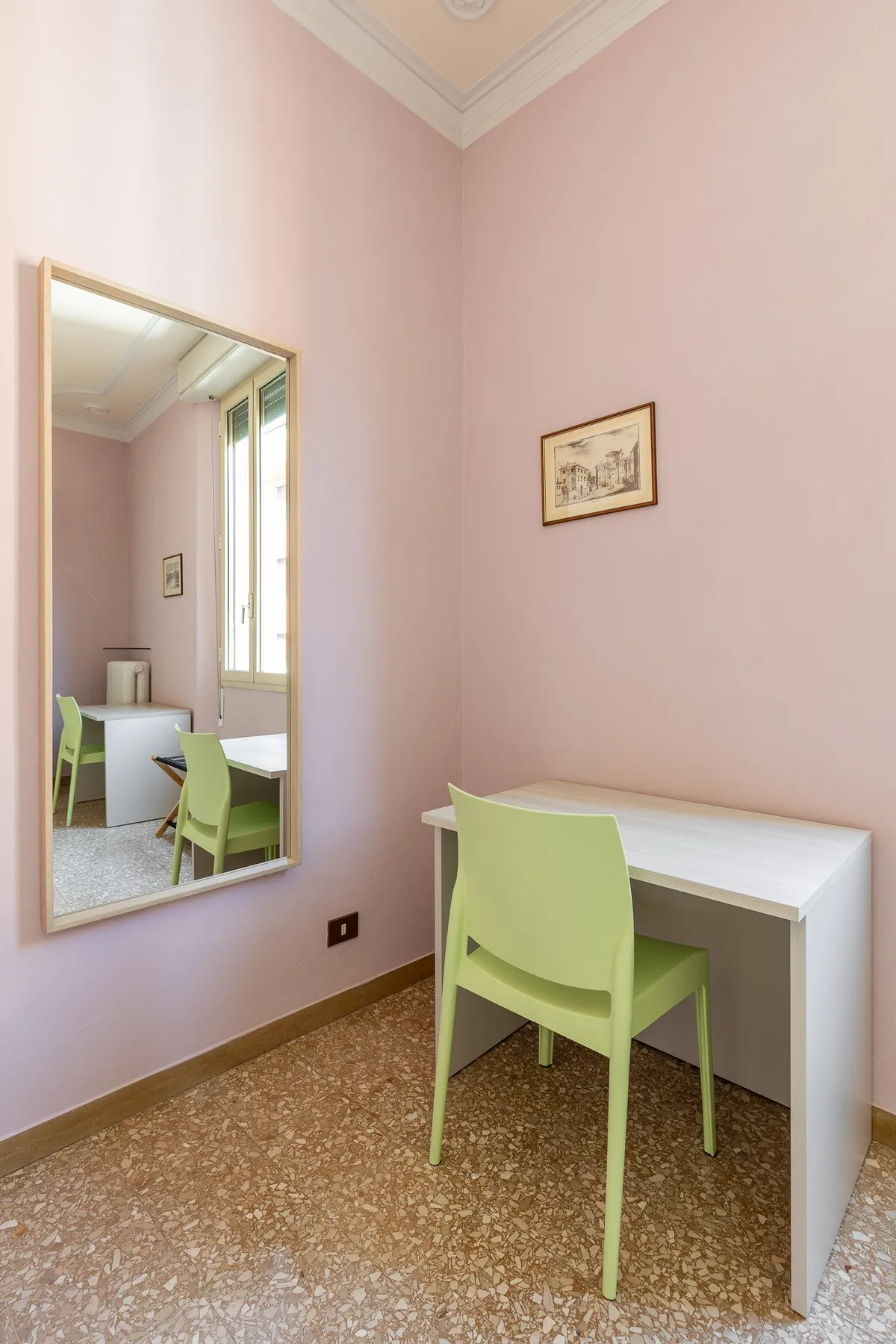 A pale pink room with a white desk and green seating.