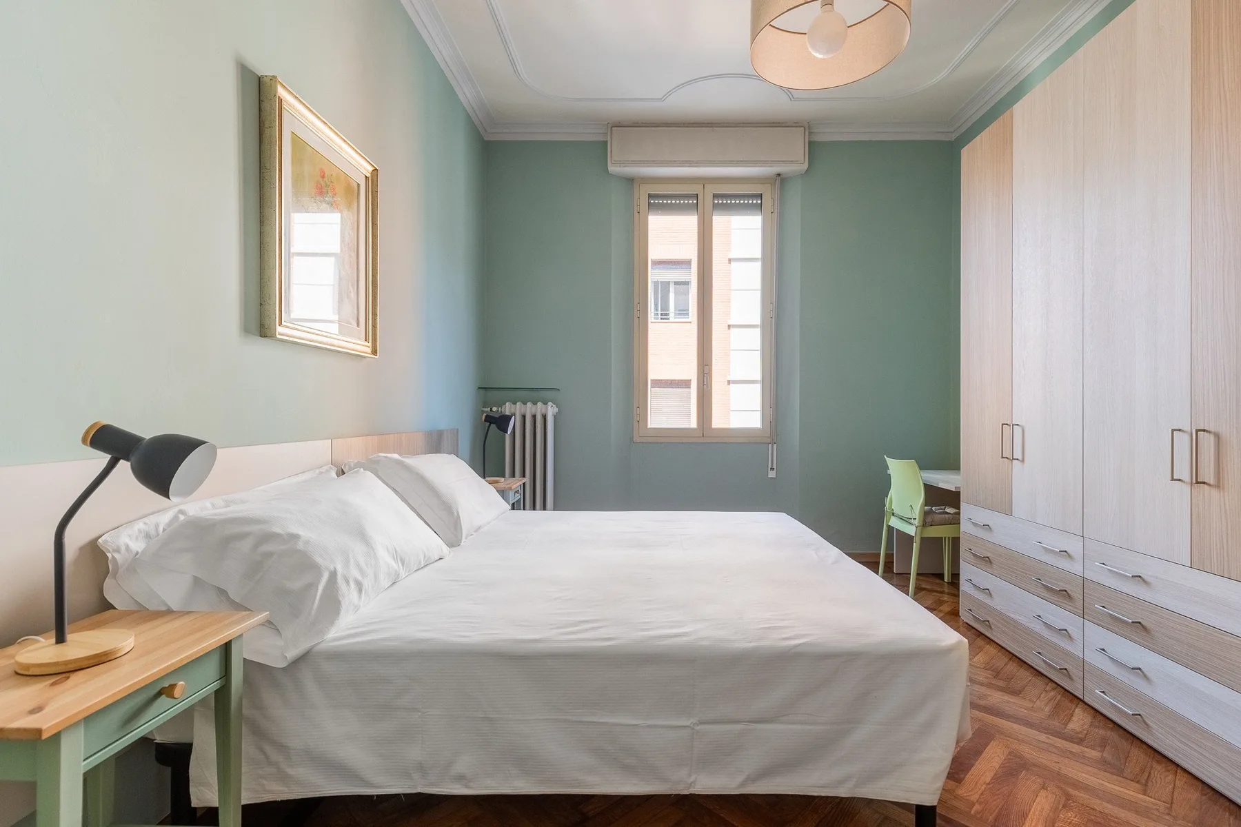 A bedroom with a bed, a window, and pale built-in wardrobes.