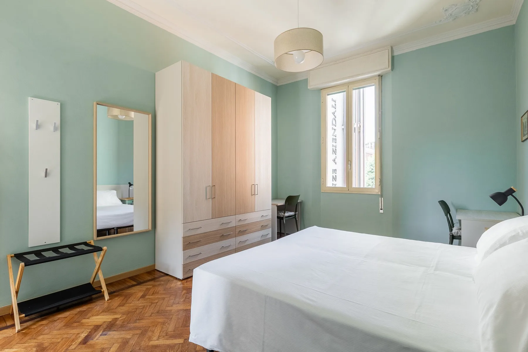 A bedroom with a white bed, pale green walls, and a large wardrobe.