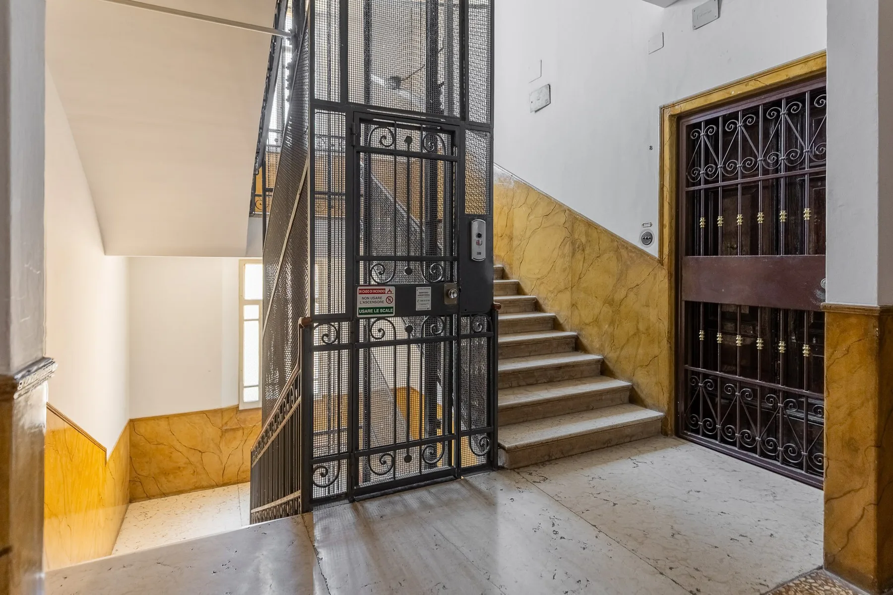 A stairwell with stone steps, a metal gate, and yellow wall panels.