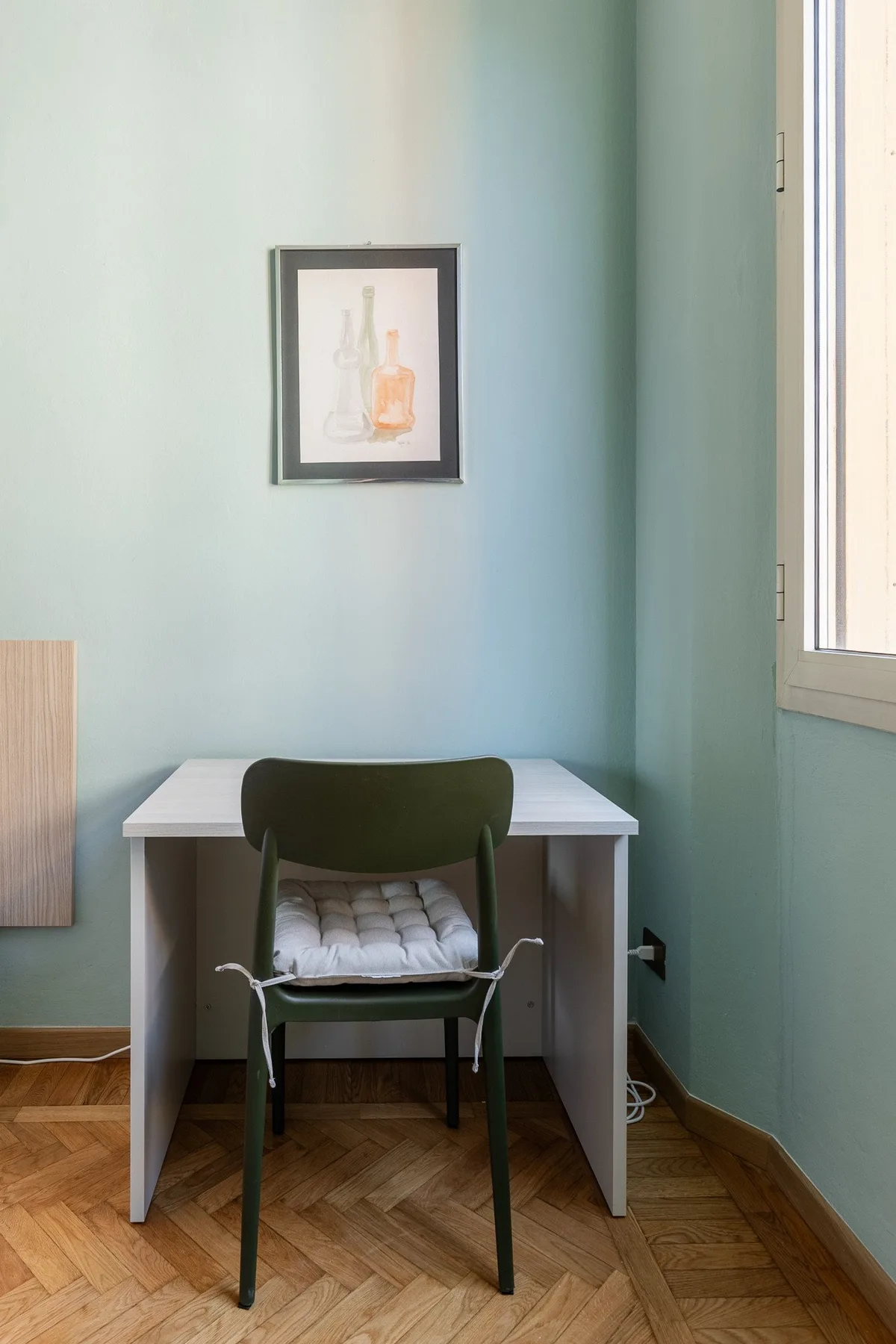 A small desk and chair sit against a pale blue wall beneath framed artwork.
