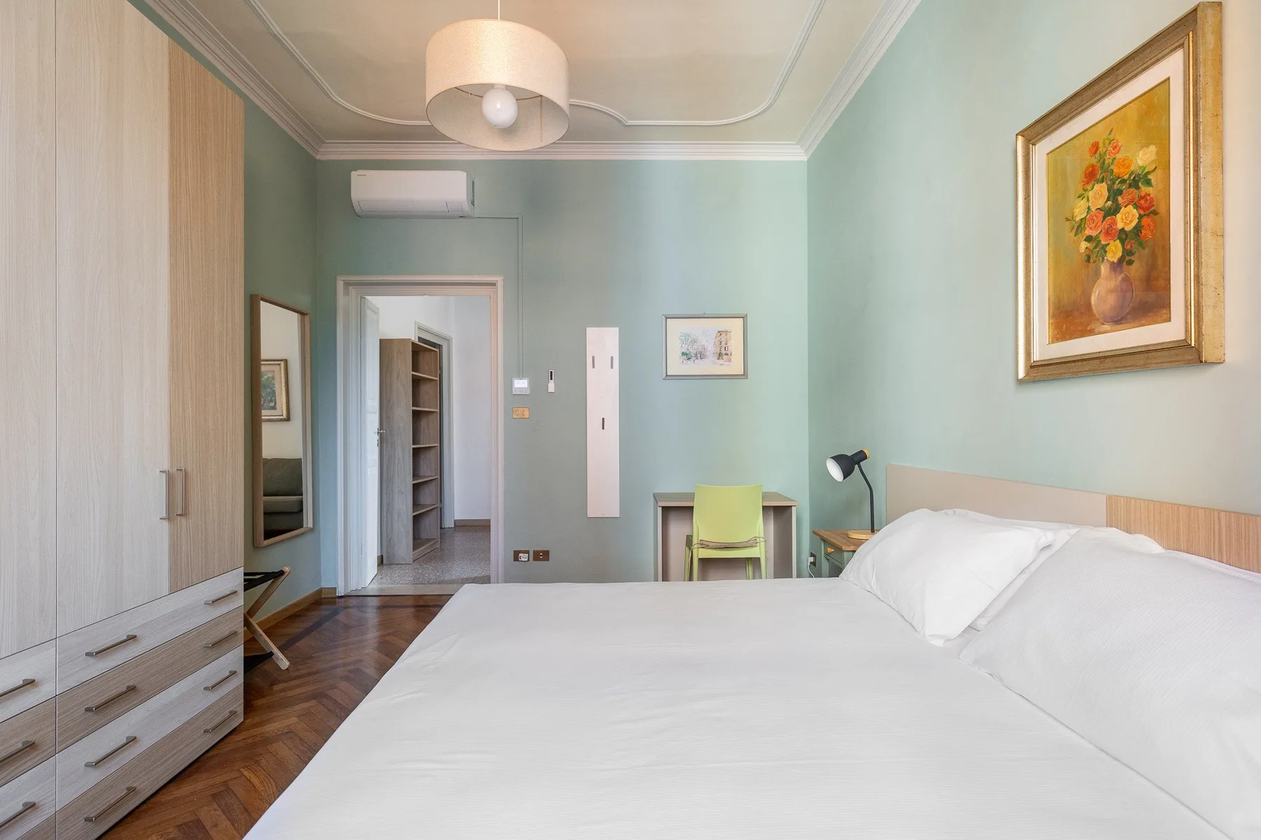 A bedroom with a large bed, pale green walls, and a desk.
