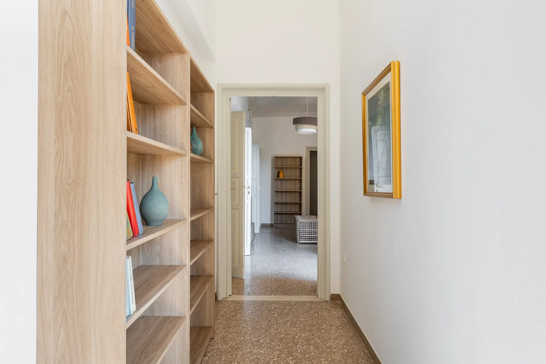 A narrow hallway with built-in shelving and an open doorway at the end.