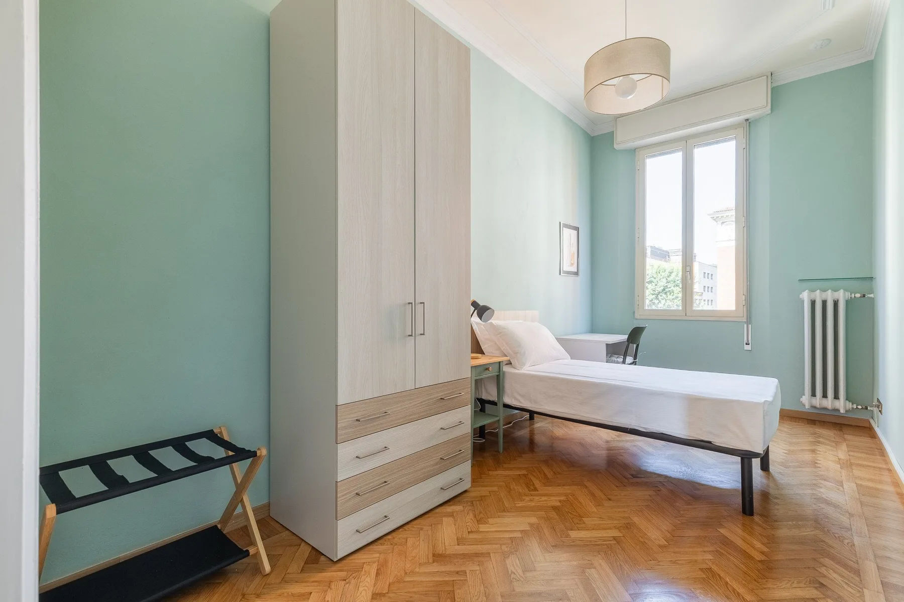 A bedroom with a bed, wardrobe, and window overlooking the street.