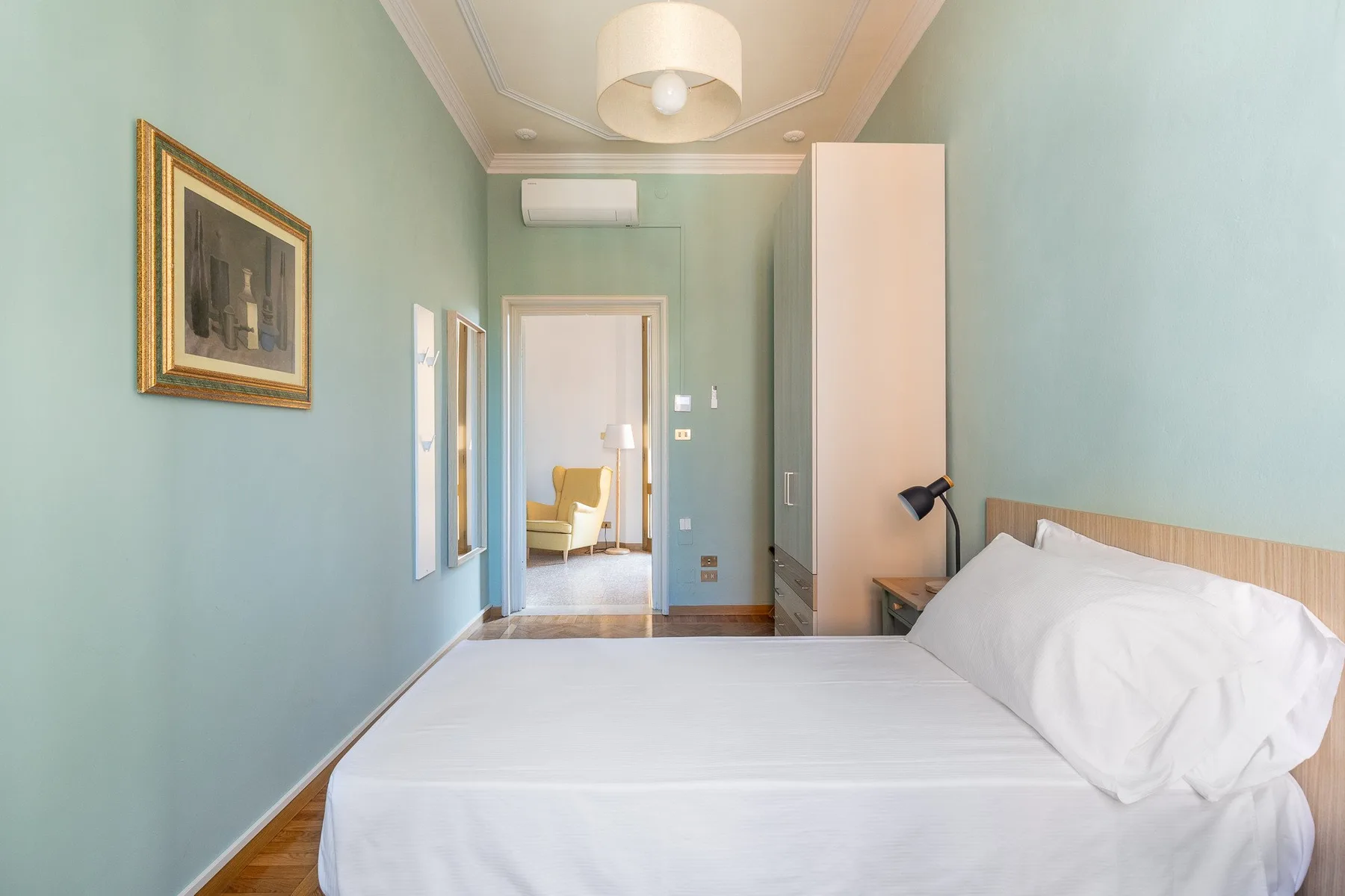 A bedroom with a neatly made bed and a doorway opening into another room.