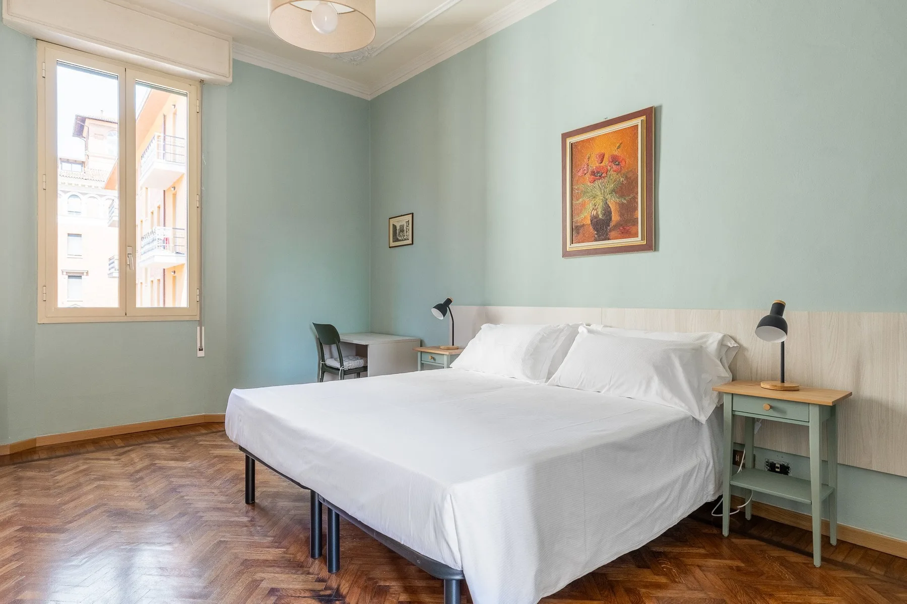 A bright bedroom with a neatly made bed, bedside tables, and a window.