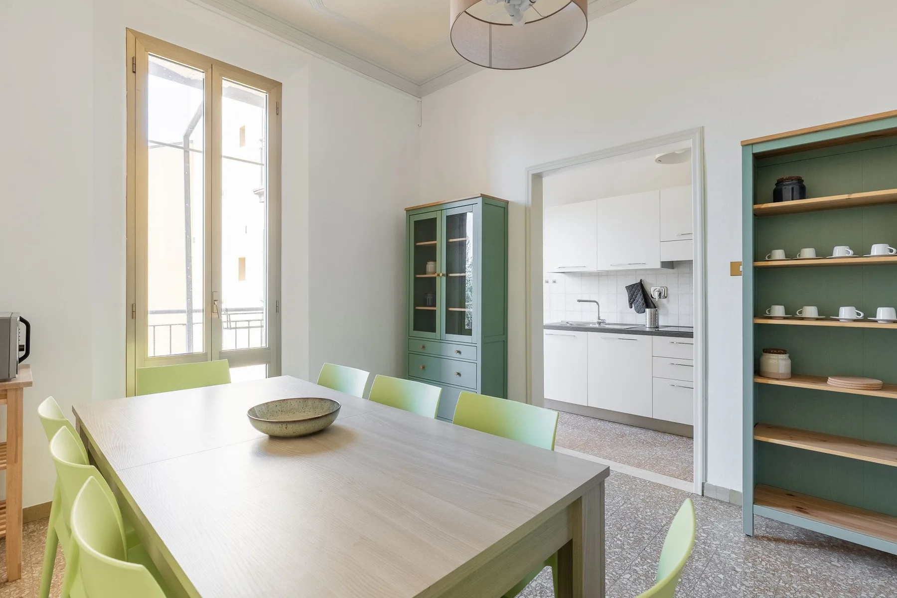 A bright dining area with a long table and a view into the kitchen.