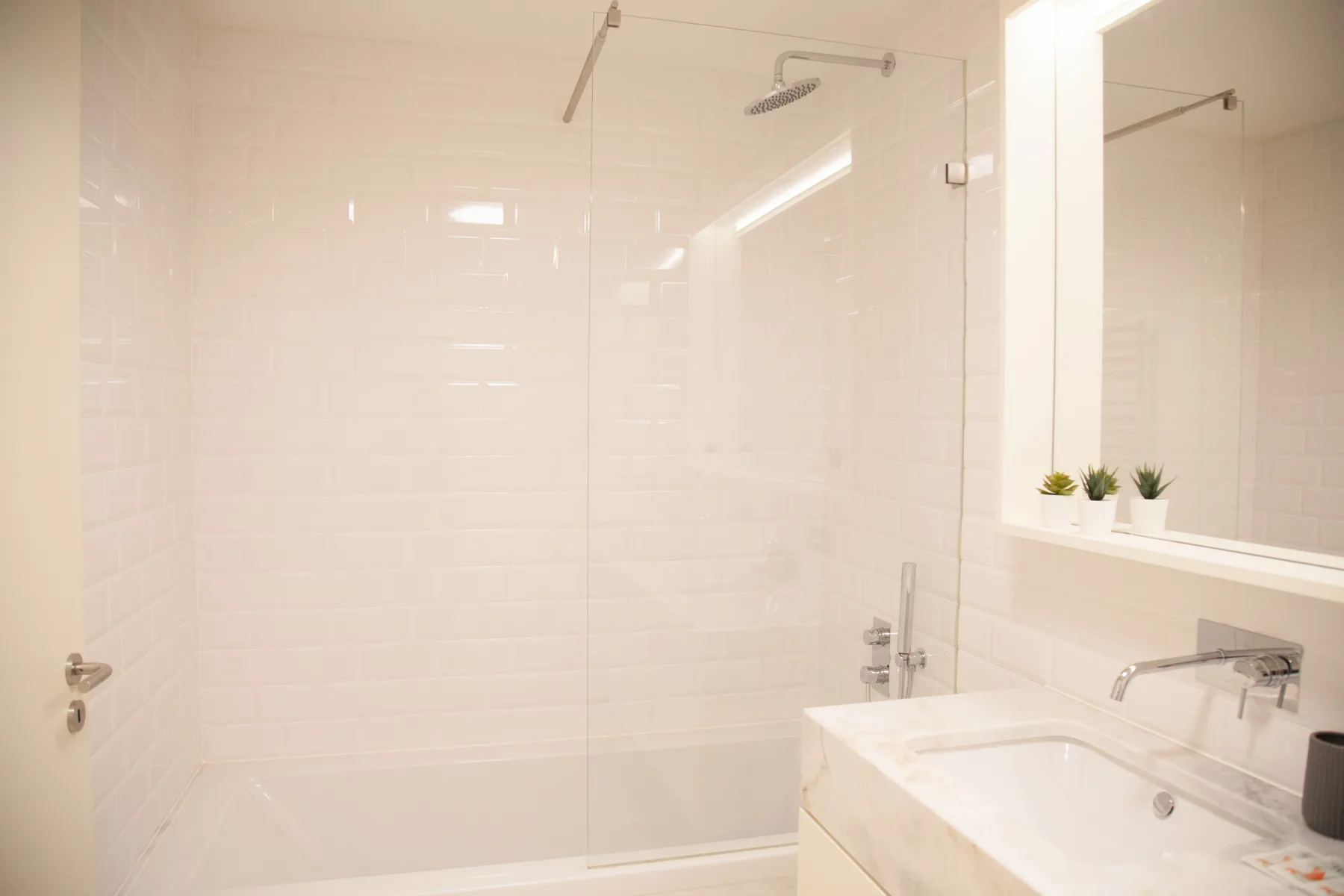 Un baño luminoso con ducha de vidrio y lavabo blanco.