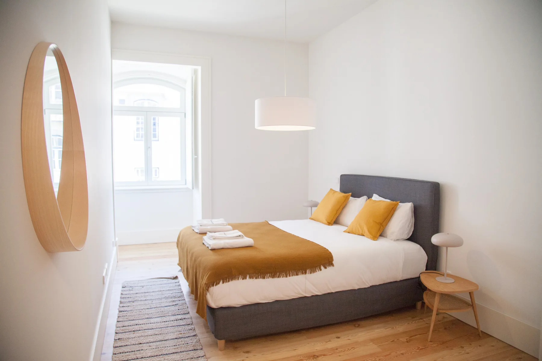 Un dormitorio luminoso con una cama doble, ropa de cama mostaza y una ventana.