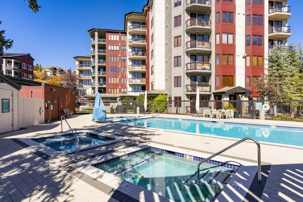 Una piscina al aire libre y una bañera de hidromasaje están junto a un edificio residencial de varias plantas.