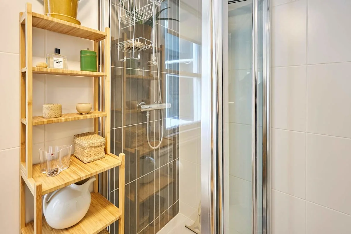A tiled bathroom with a shower and wooden shelving.