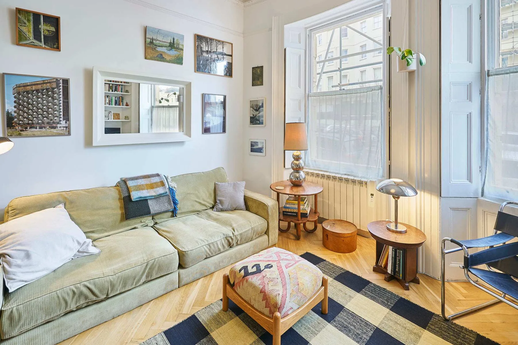 A bright living room with a sofa, framed pictures, and large windows.