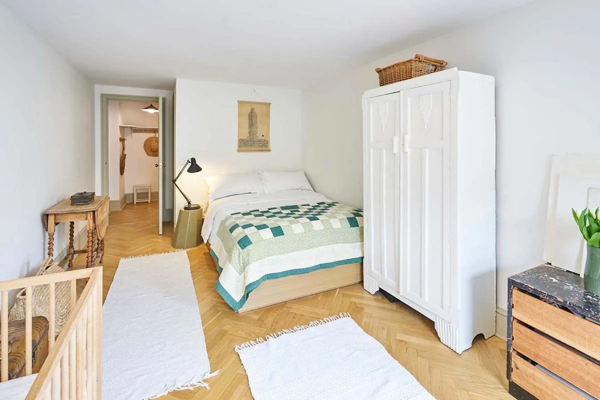 A bright bedroom with a bed covered by a green-and-white quilt.